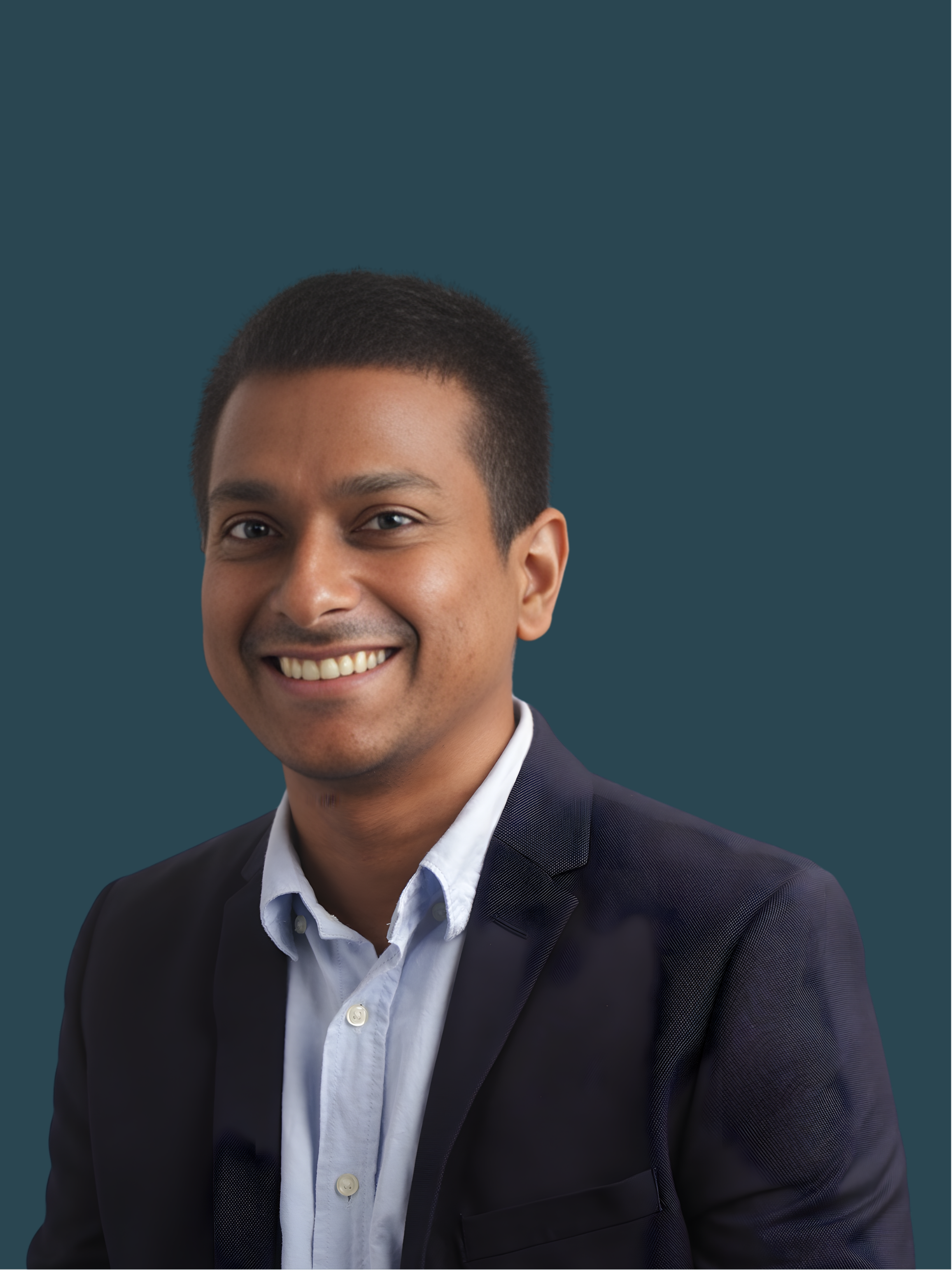 A smiling young man with short black hair, wearing a white shirt and a dark blazer, against a solid dark teal background.