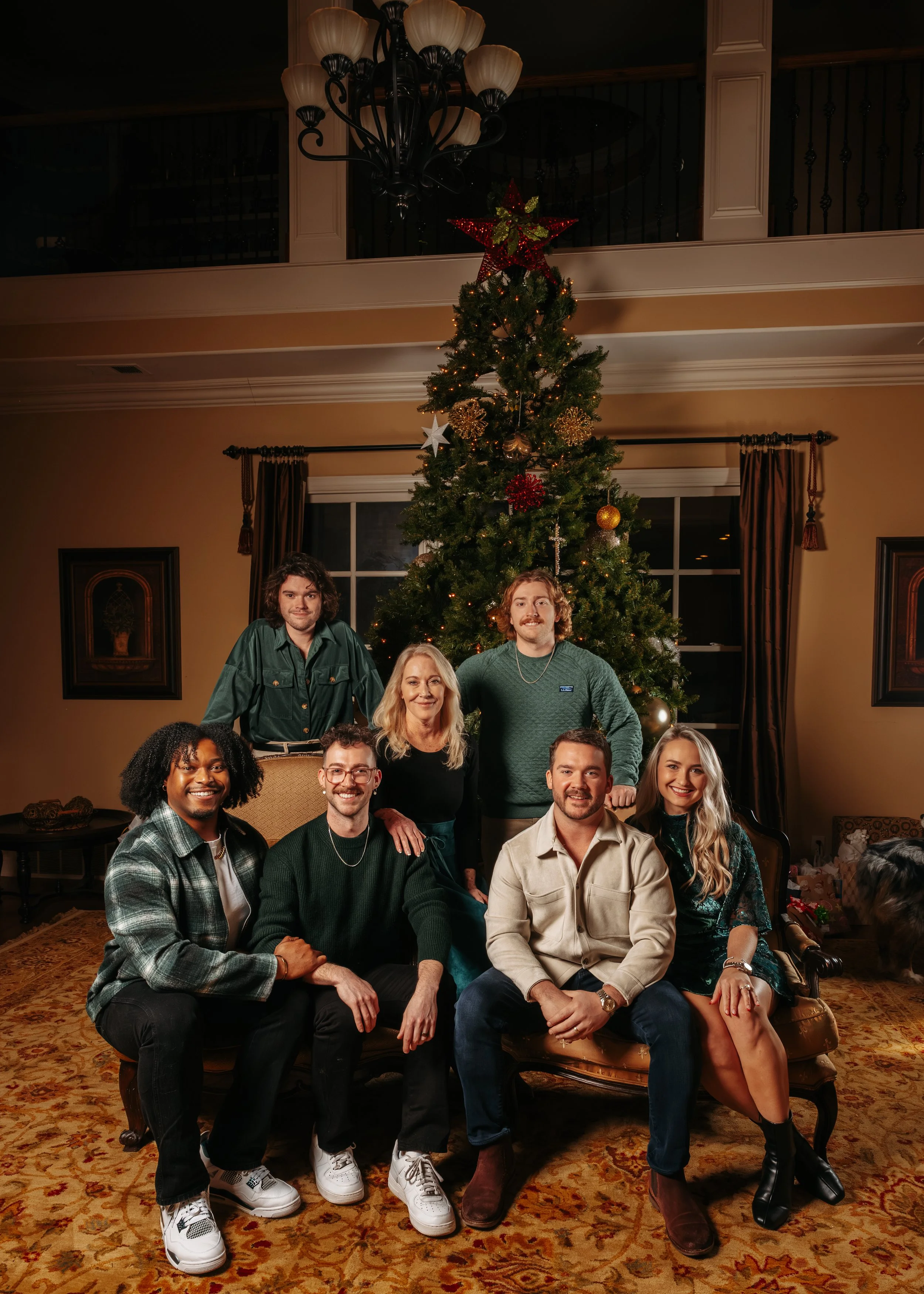 A family of seven posing in front of a decorated Christmas tree in a cozy living room.