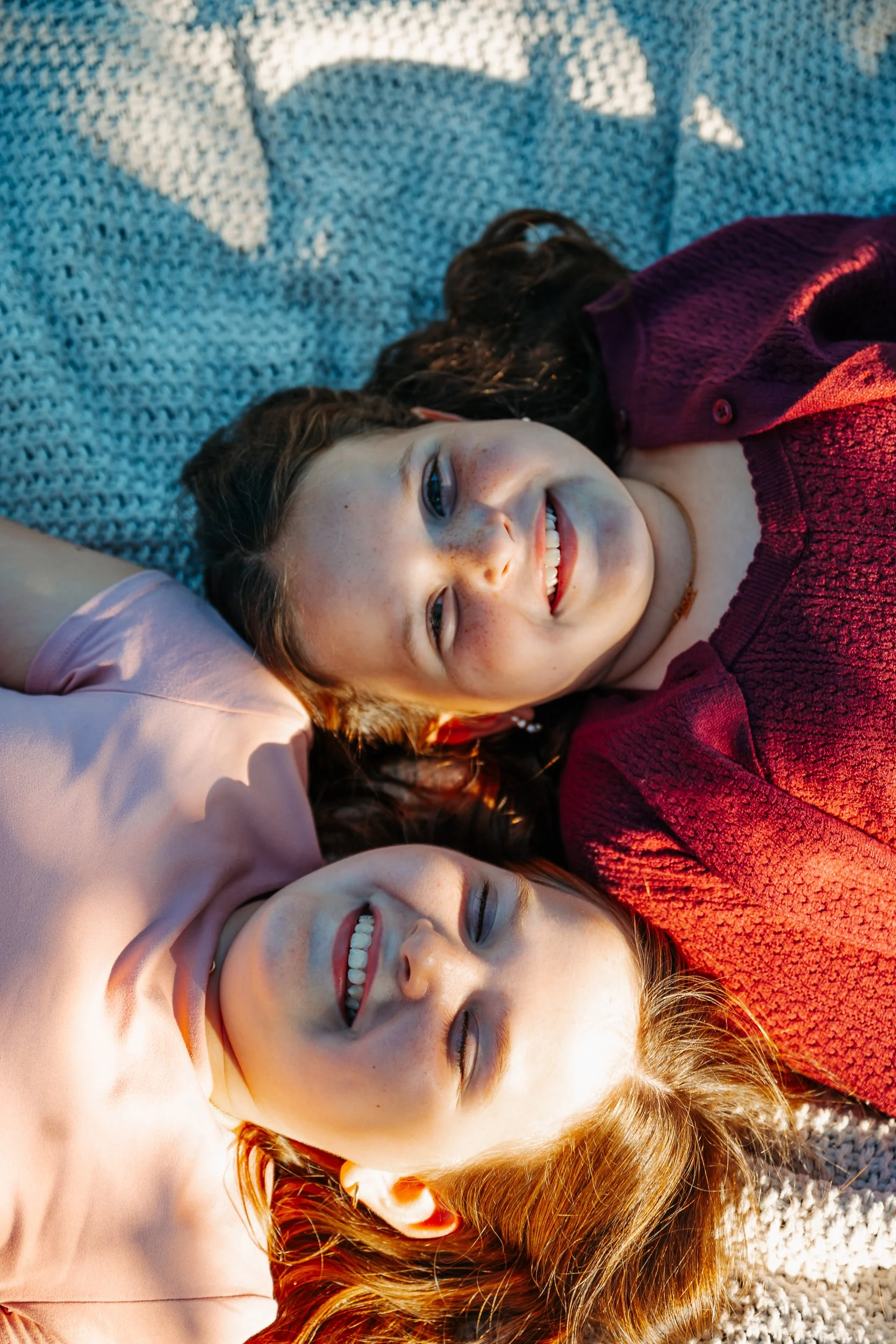 Two young women lying on a textured blanket, smiling and enjoying the sunlight.