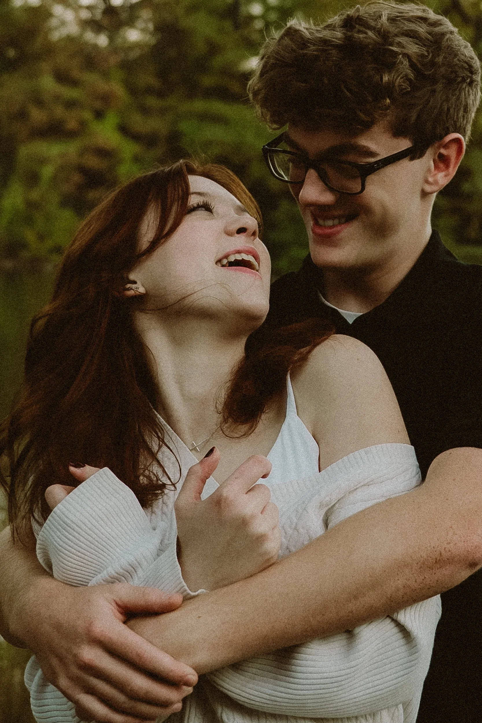 A young couple embrace outdoors, smiling and looking into each other's eyes.