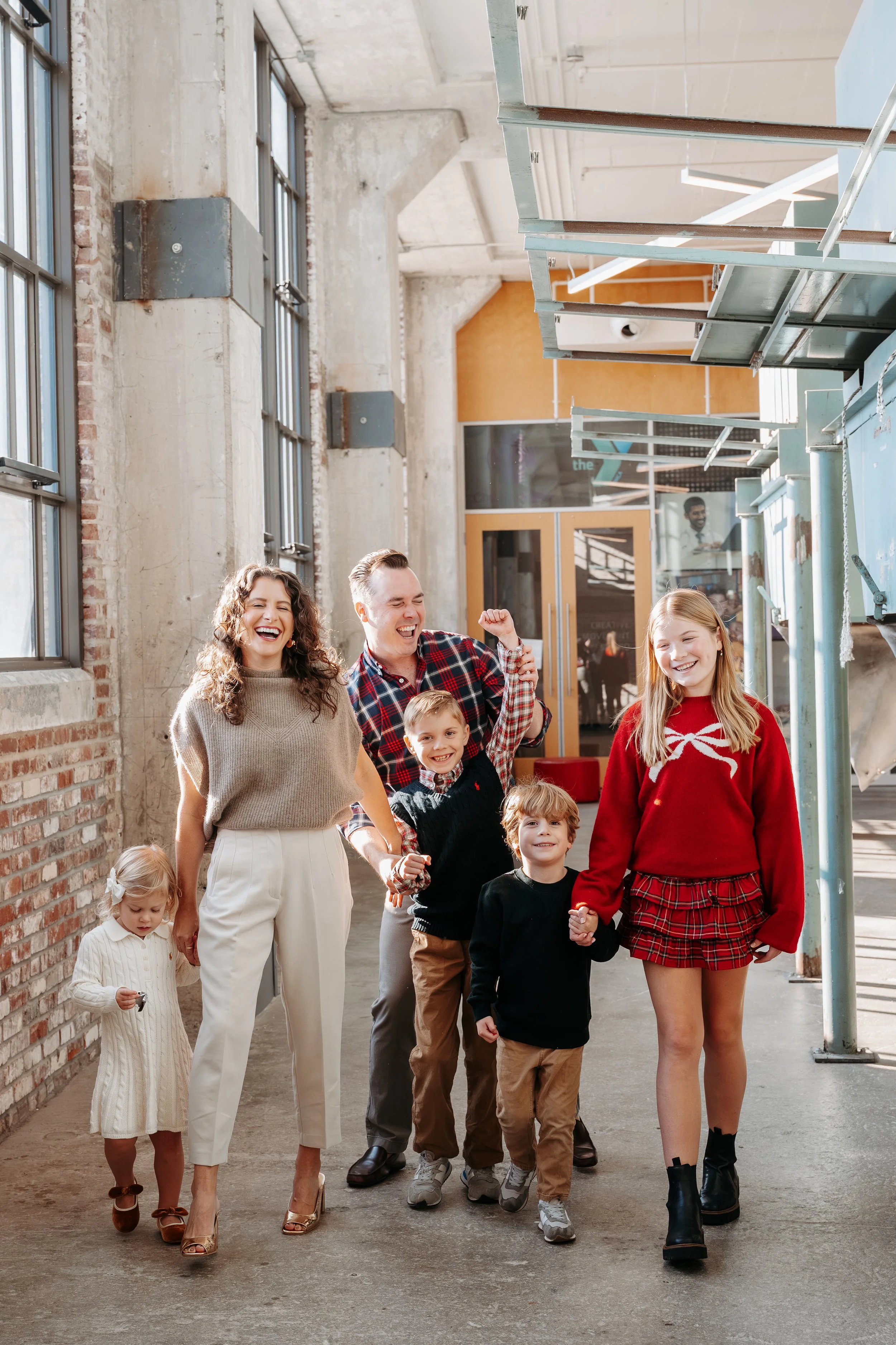 Family of six, including three children, walking and laughing inside an industrial-style building with exposed brick and windows, during daytime.