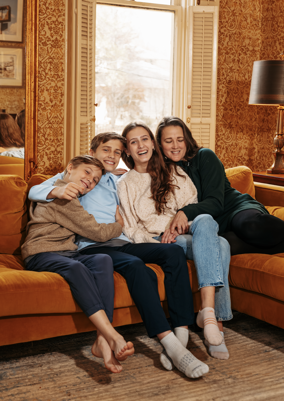 Four people sitting on an orange couch in a cozy living room, smiling and hugging each other.