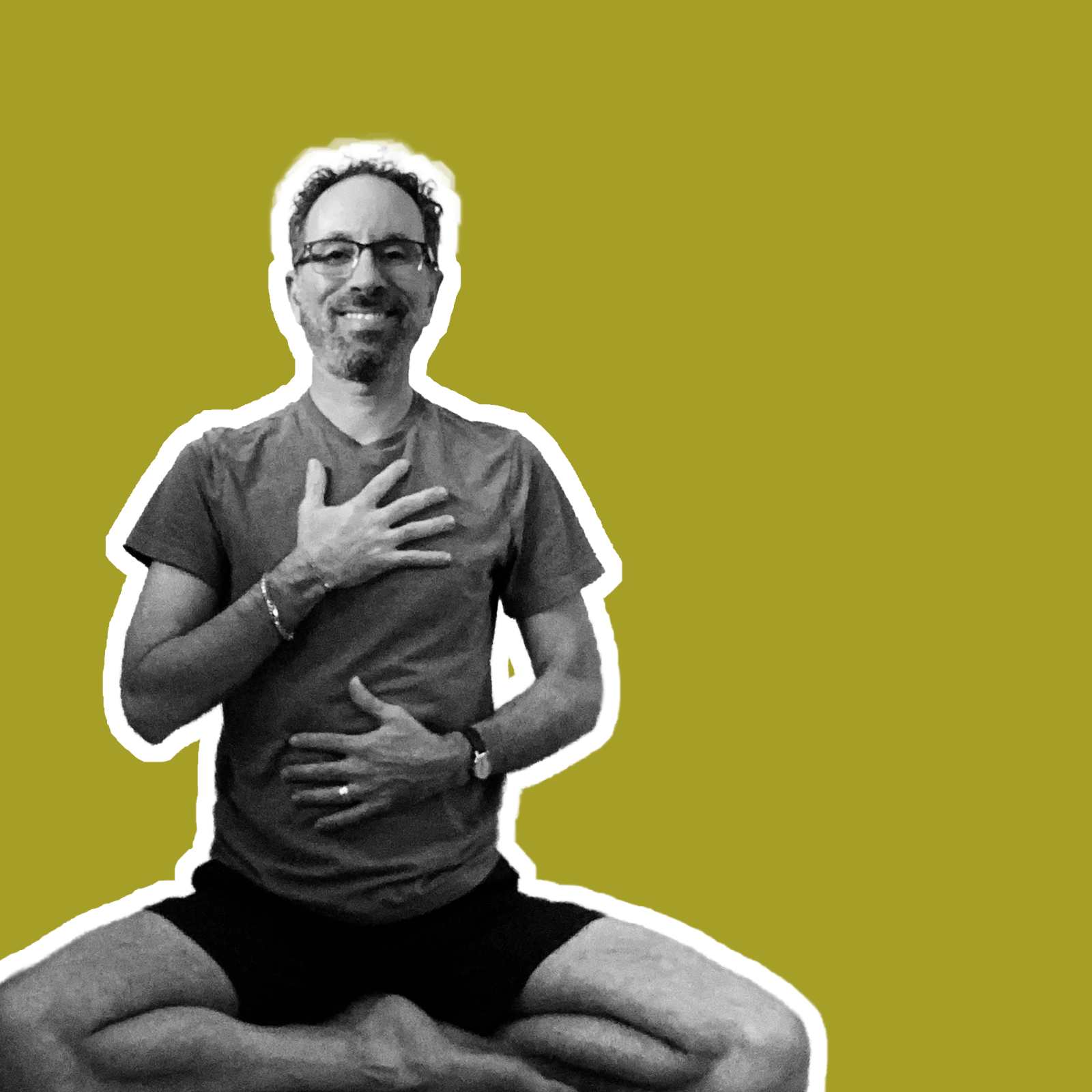 A man with glasses and a beard, smiling, sitting cross-legged in a yoga pose on a solid green background. He is wearing a t-shirt and shorts, with one hand on his chest and the other on his stomach.