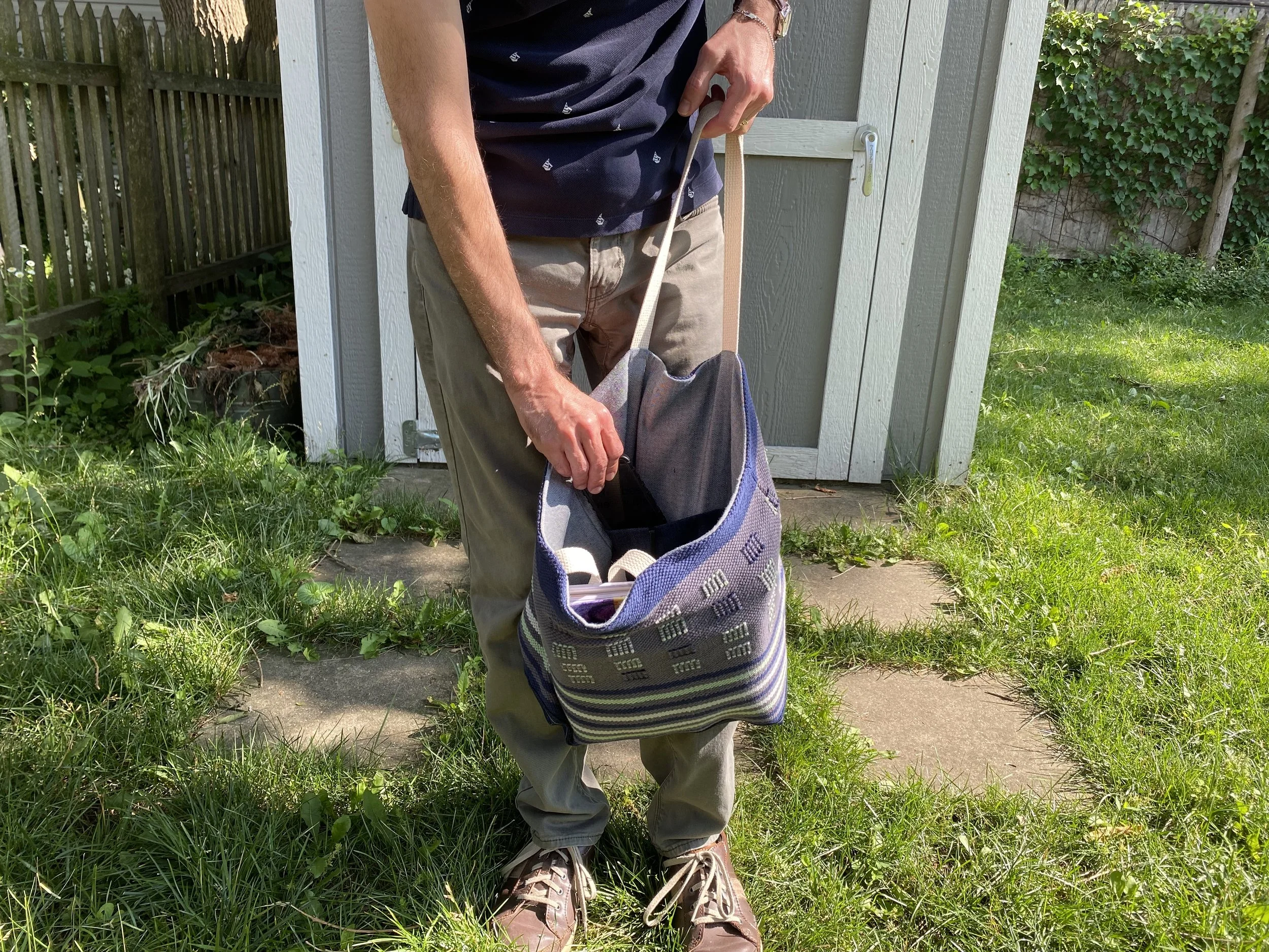 Person standing outside on grass, holding a striped bag.