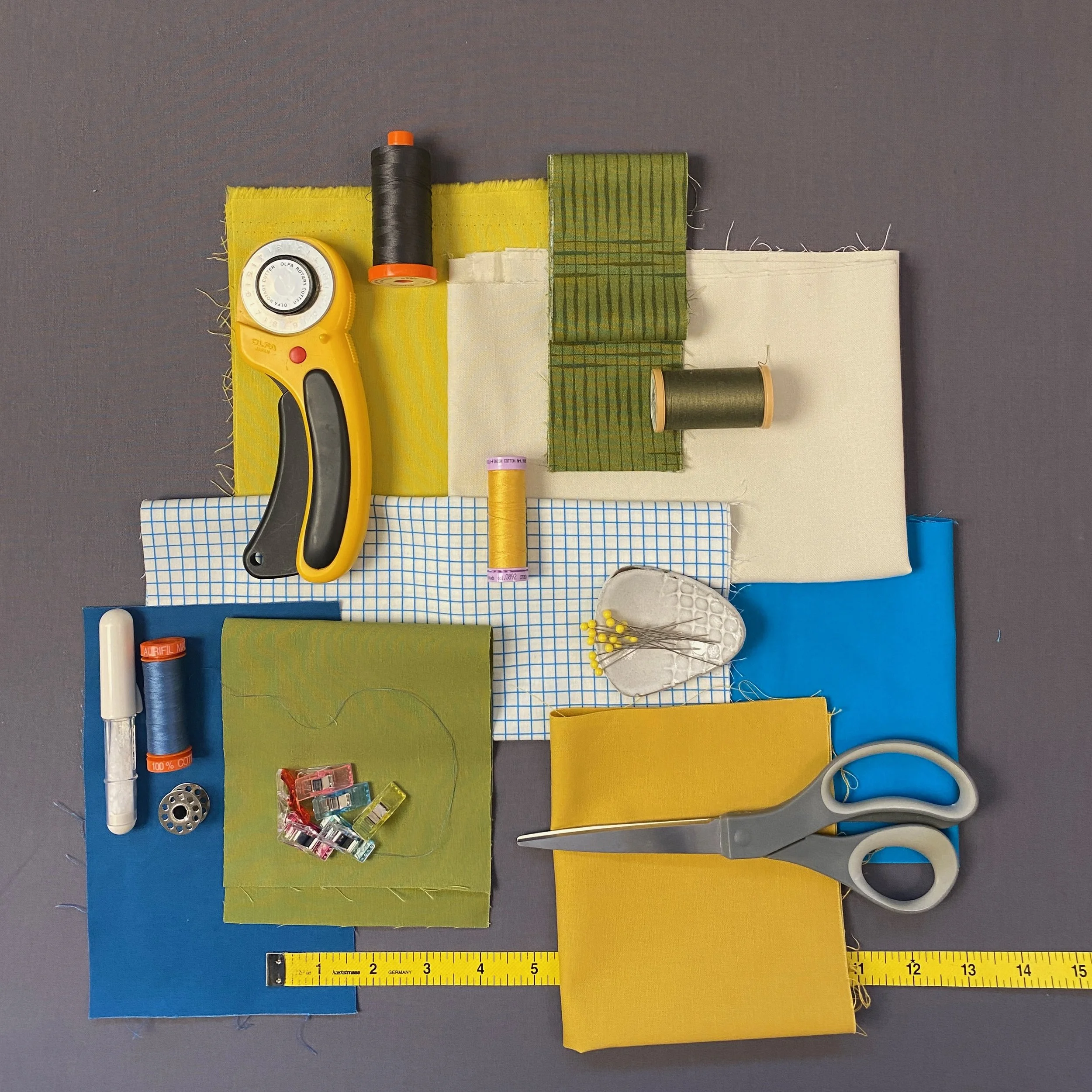 Collection of sewing tools and fabric swatches on a gray background, including scissors, thread spools, sewing patterns, clips, and a measuring tape.