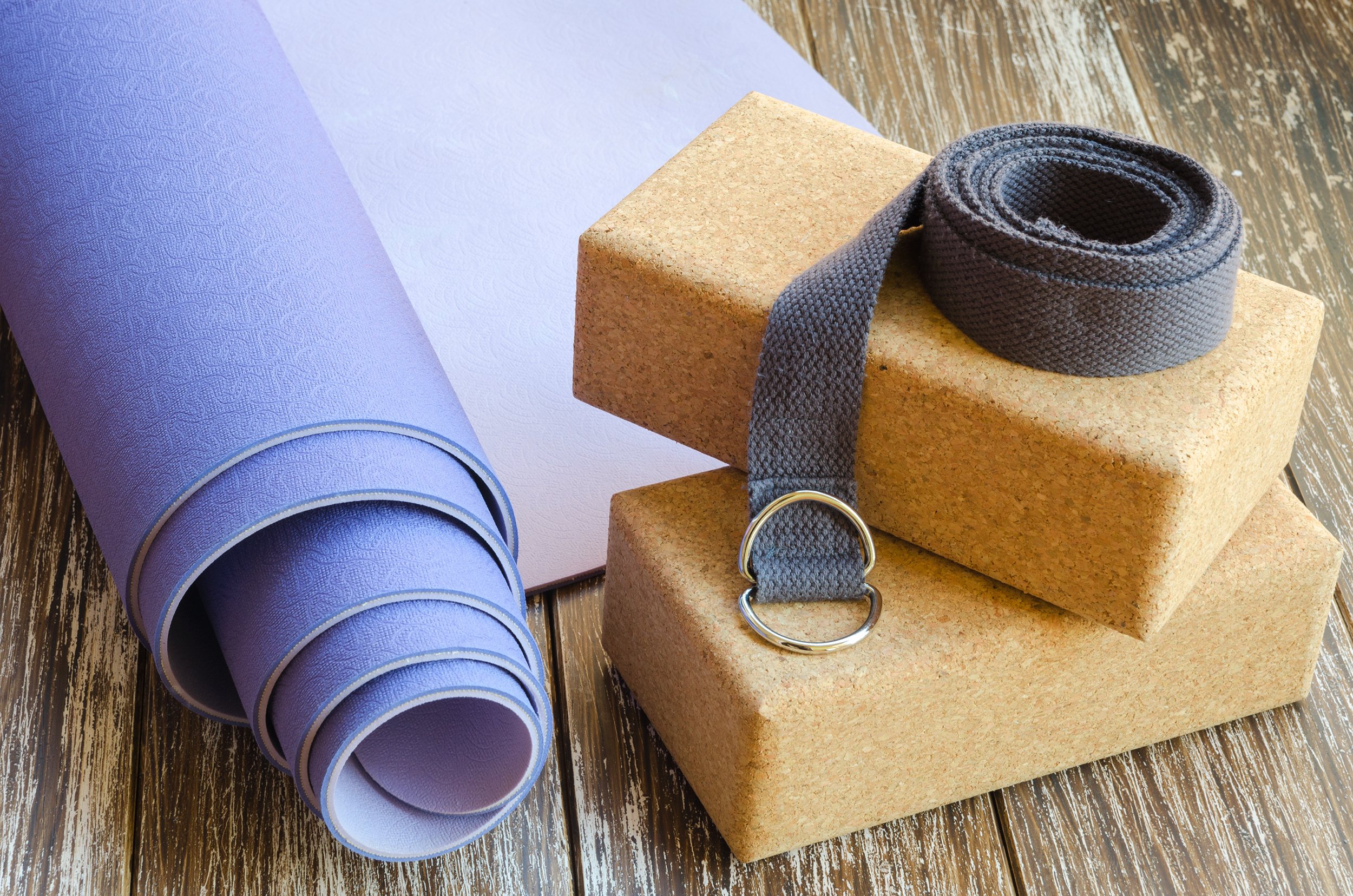 Yoga mat, yoga blocks, and a yoga belt on a wooden floor.