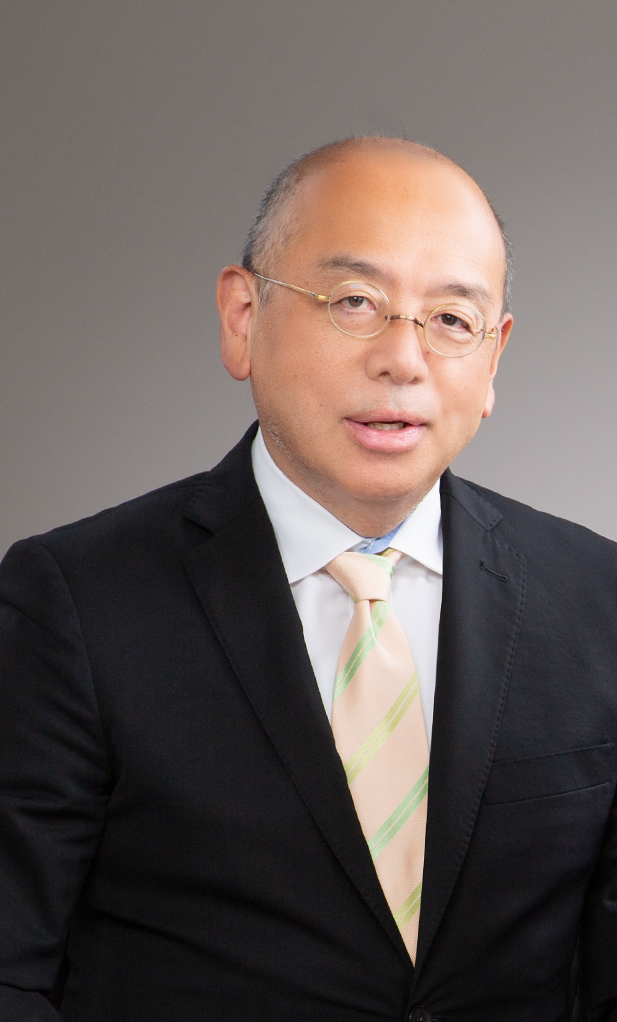 A middle-aged man with glasses and a bald head wearing a black suit, white shirt, and a pastel plaid tie, posing against a plain gray background.
