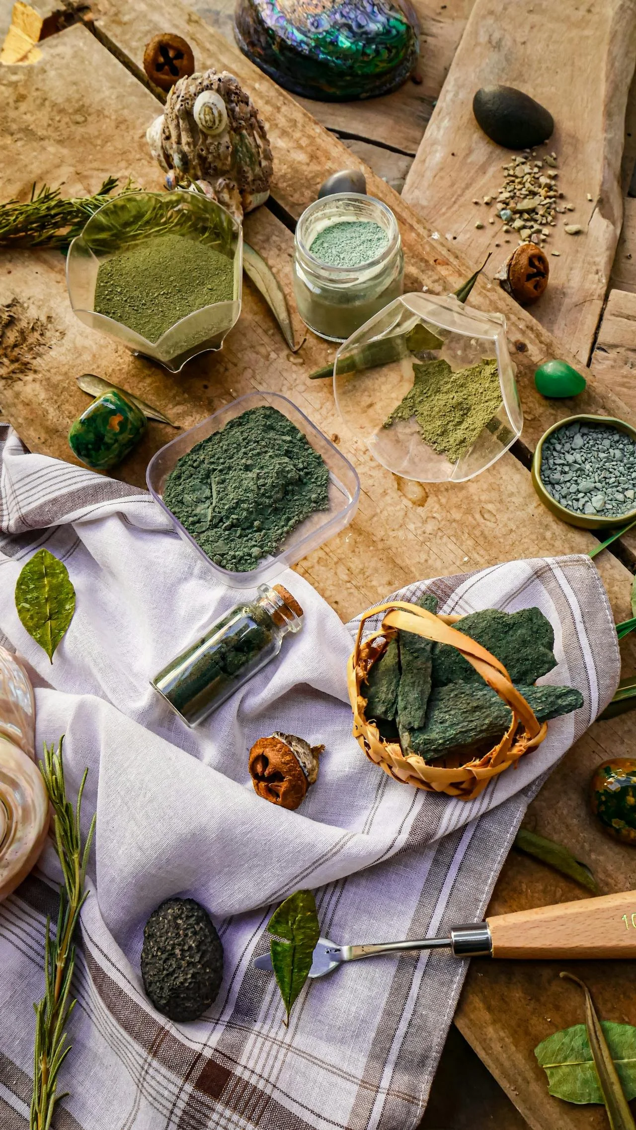 Divers poudres vertes, galets, plantes et objets naturels sur une table en bois, évoquant la nature ou la spiritualité.