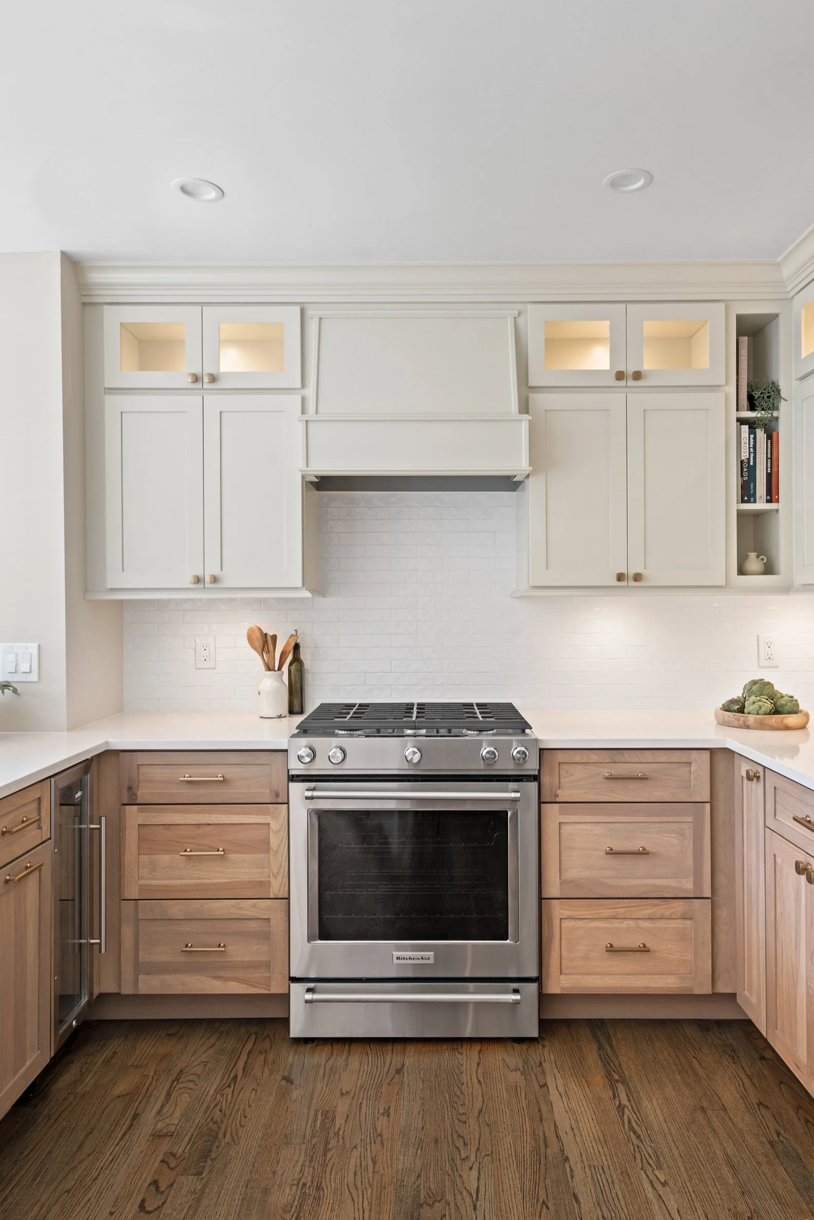 Kitchen with white upper cabinets, light wooden lower cabinets, stainless steel stove, and hardwood floor.