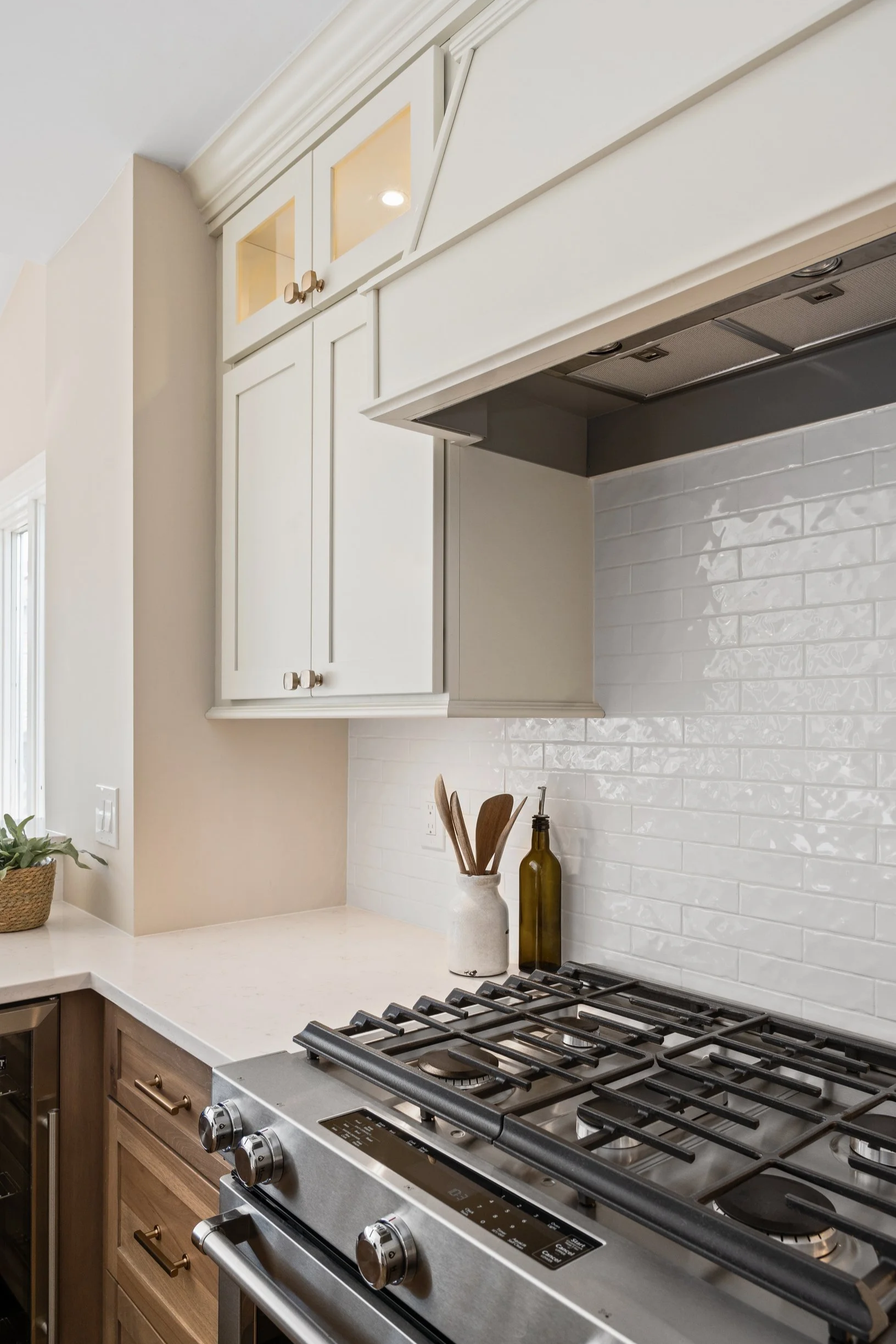 Kitchen with white upper cabinets, beige lower cabinets, a stainless steel gas stove, decorative knife holder, and a small potted plant on the counter.