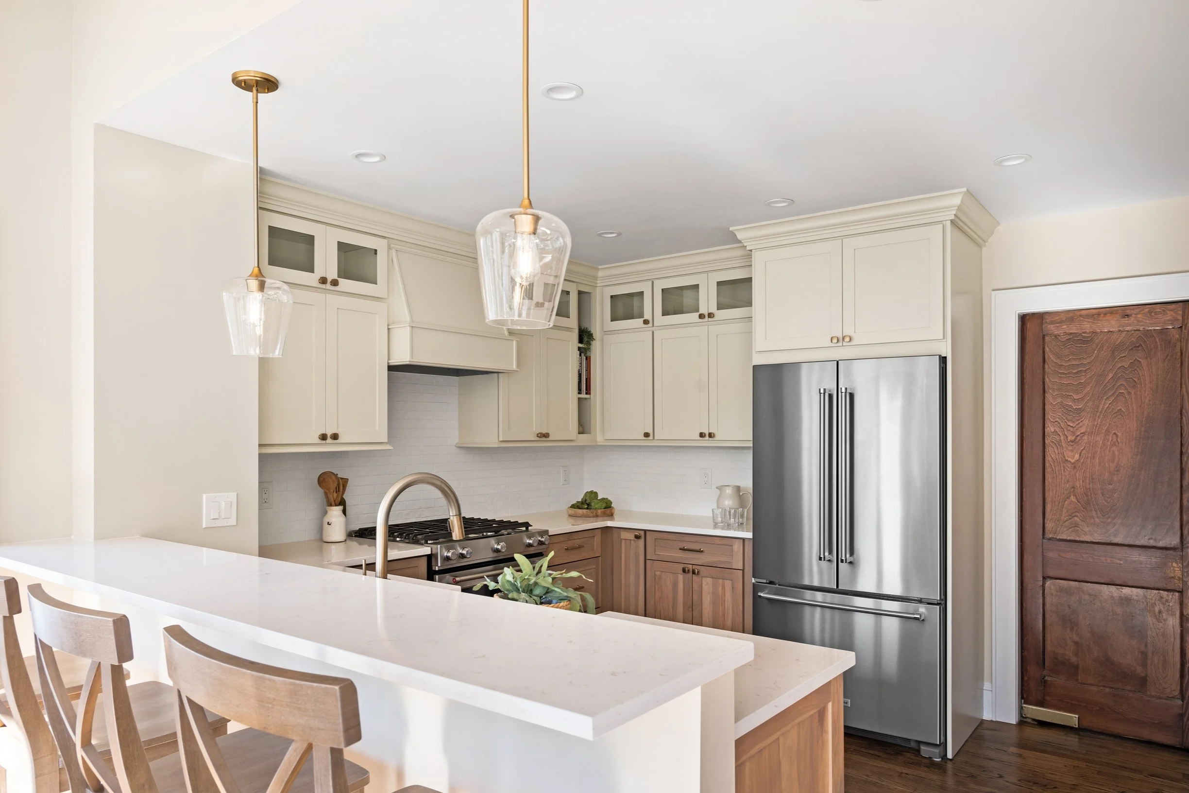 Modern kitchen with beige cabinets, stainless steel refrigerator, white countertops, and wooden accents.