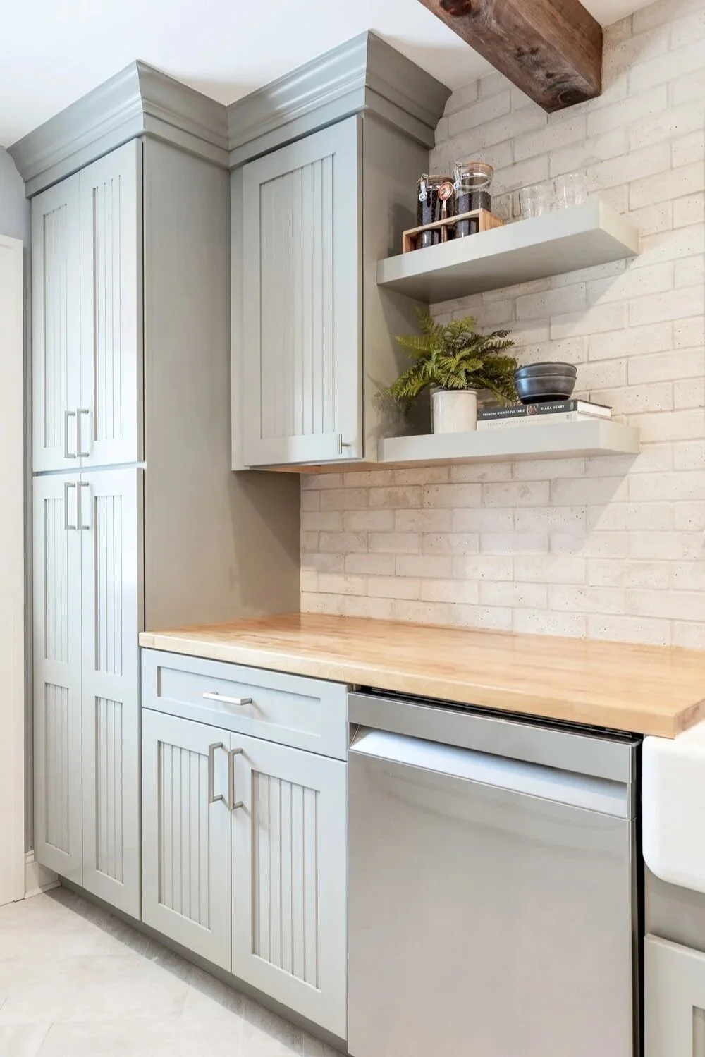 Kitchen with white cabinets, wood countertop, brick wall, open shelves with jars, plant, and books.