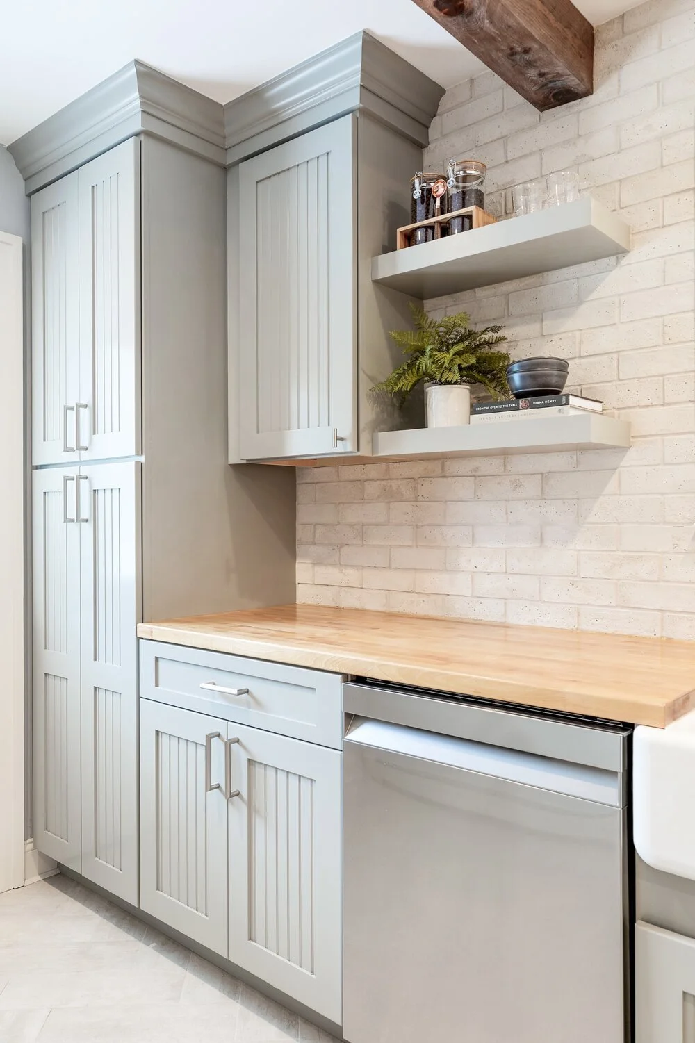 Kitchen with white cabinets, wood countertop, brick wall, open shelves with jars, plant, and books.