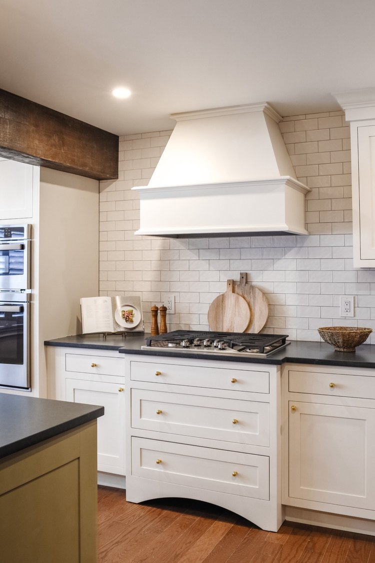 Kitchen with white cabinets, black countertops, a stove, a white range hood, cutting boards, a cookbook, and decorative items.