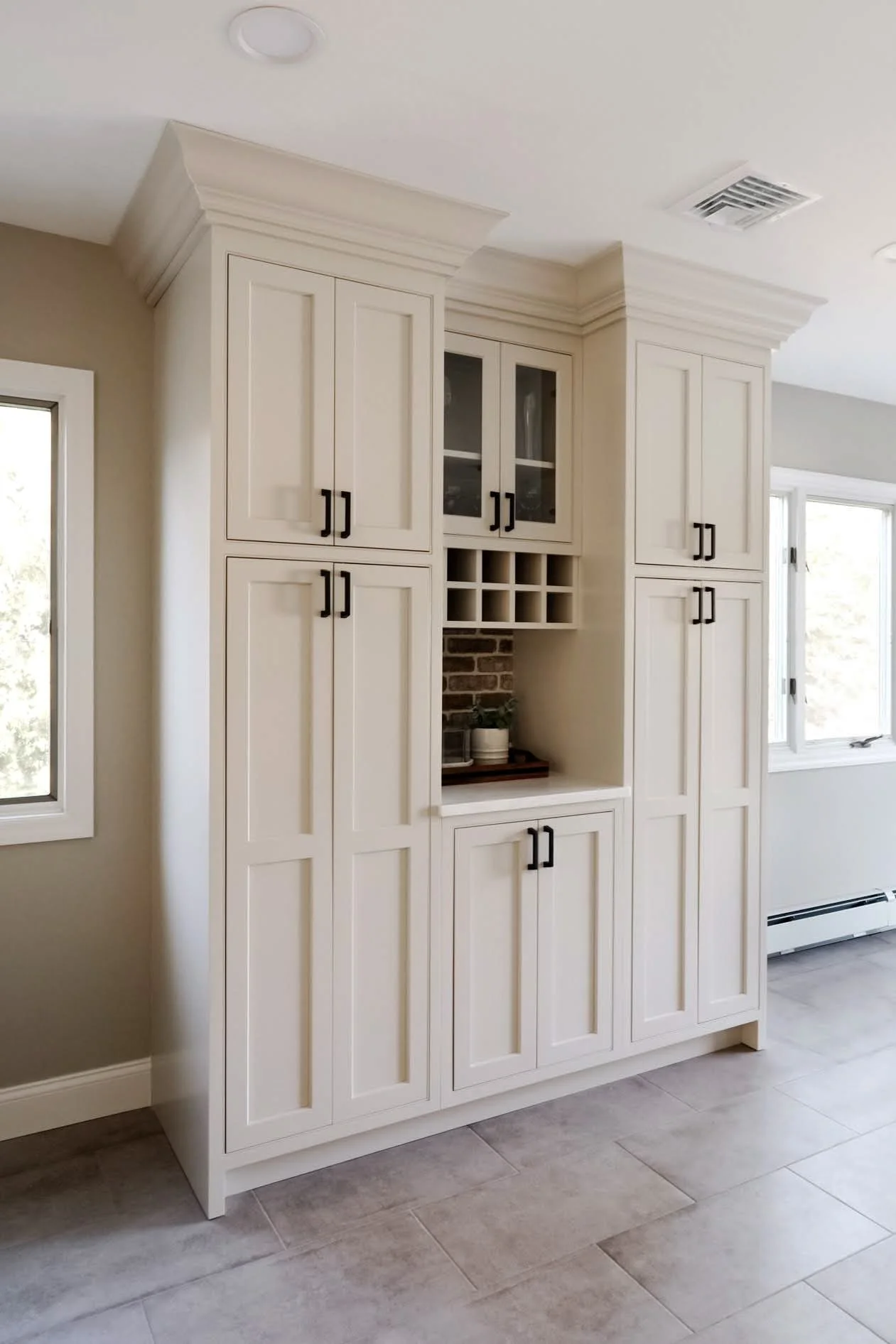 White kitchen cabinet with multiple doors, a glass-front display section, and wine bottle compartments, against a beige wall with a window nearby.