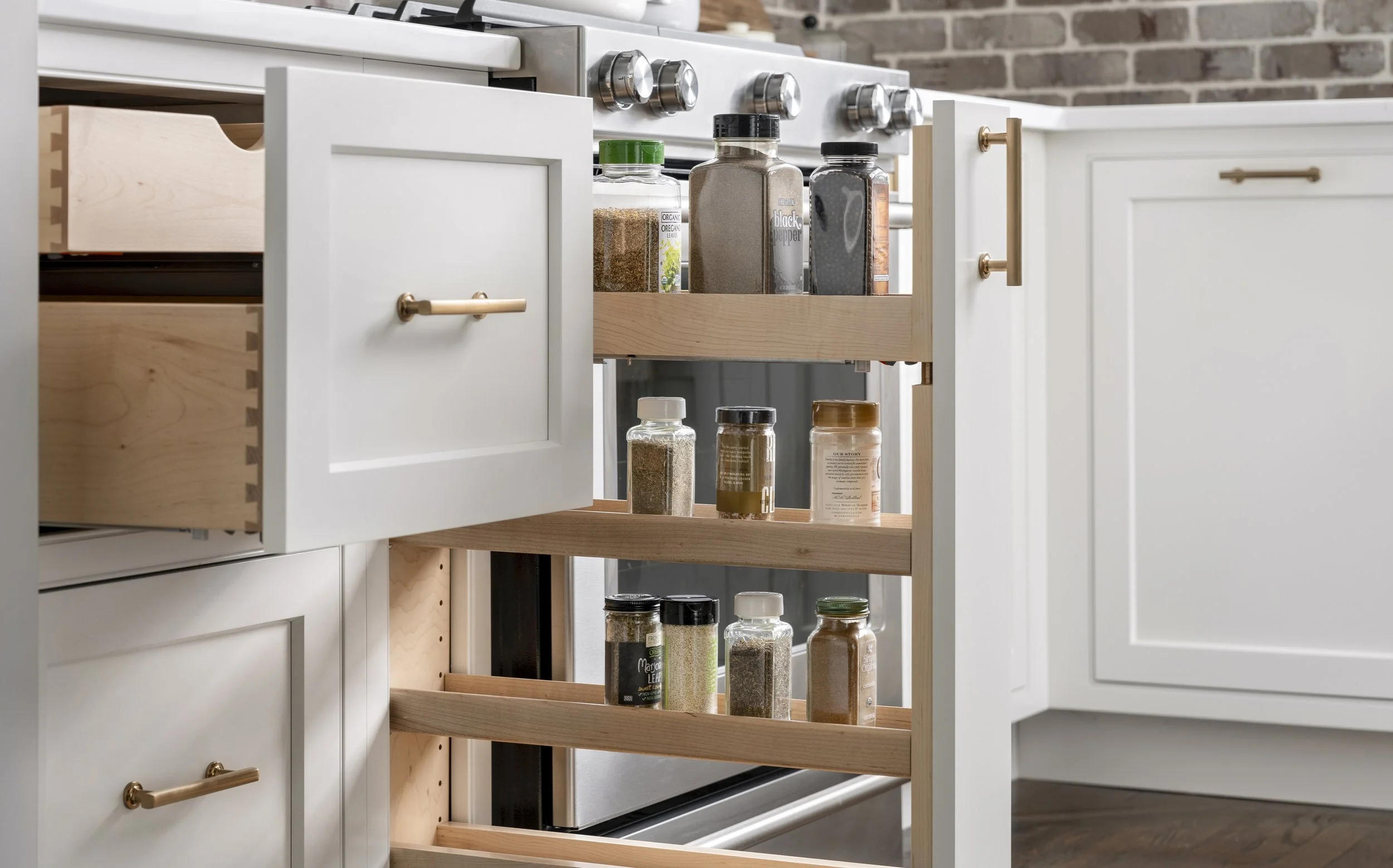 Kitchen cabinet with open shelves filled with spices and seasonings in jars and bottles, with a brick wall in the background.