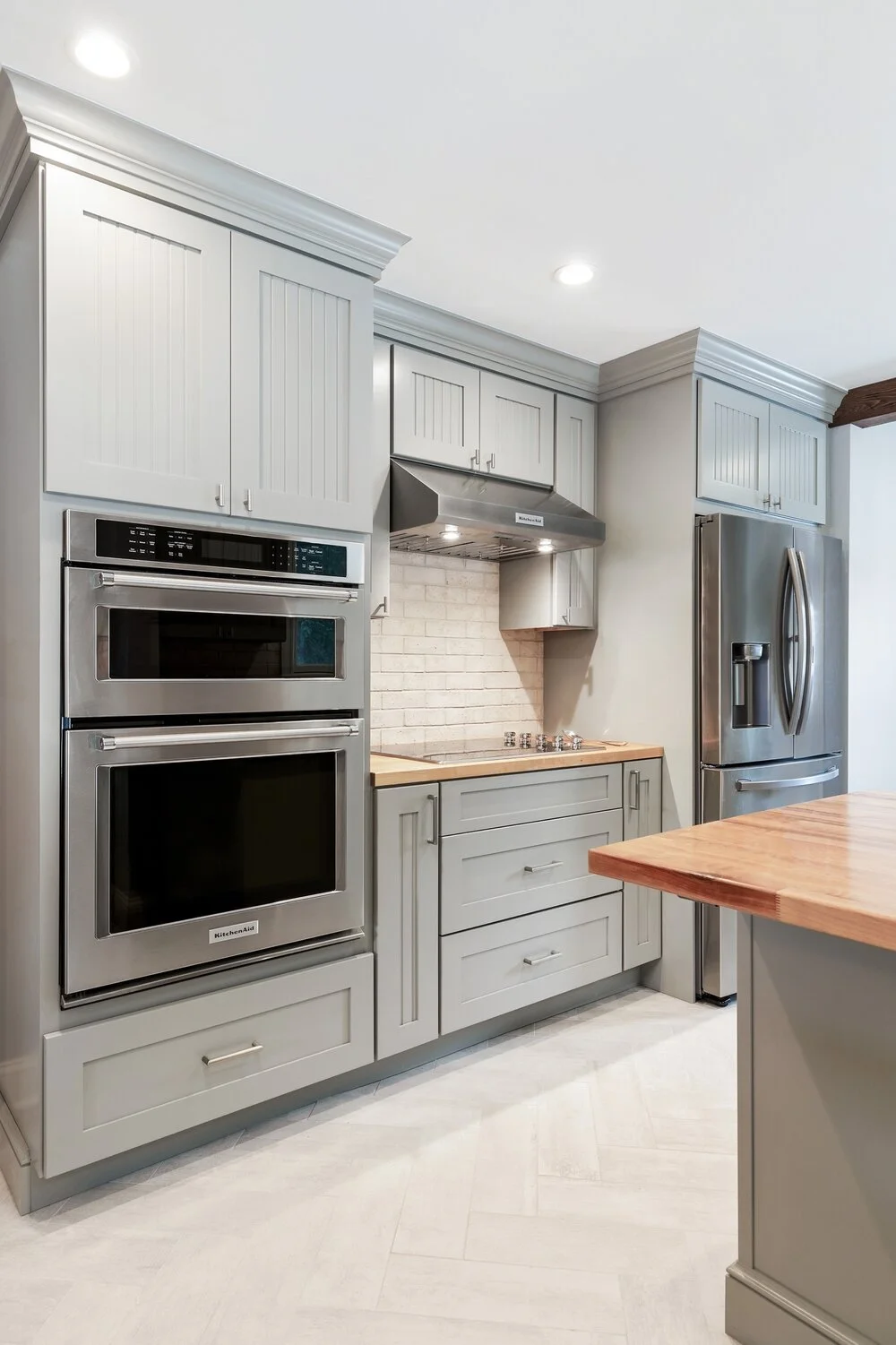 Modern kitchen with white cabinetry, stainless steel appliances, a brick backsplash, and a wooden countertop island.
