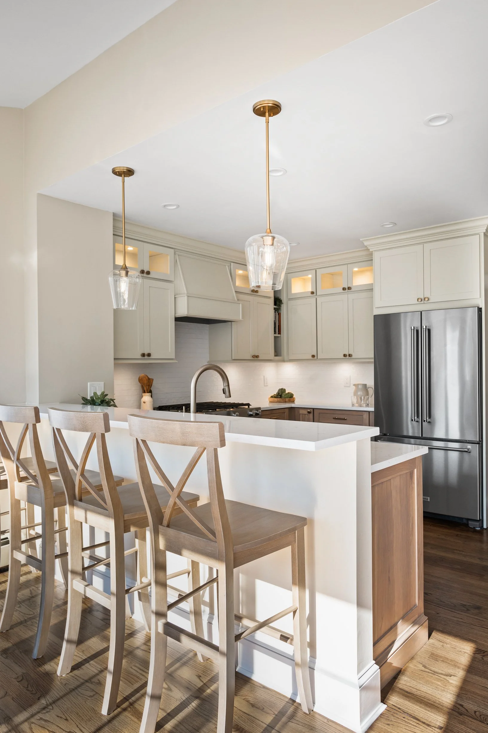Modern kitchen with white cabinets, stainless steel refrigerator, and a white countertop island with four wooden barstools.