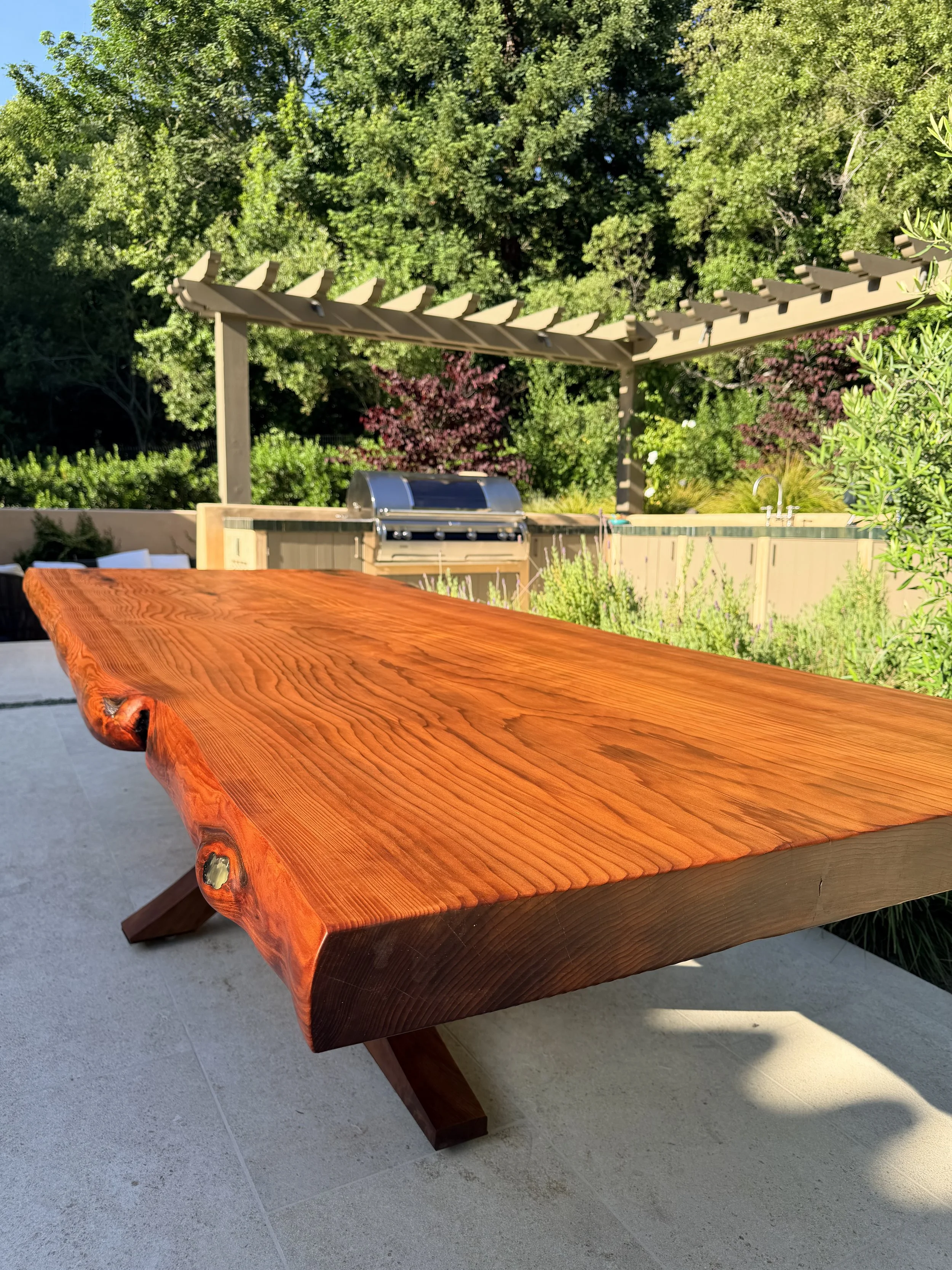 A wooden outdoor table with a natural, polished surface, supported by two angled legs.