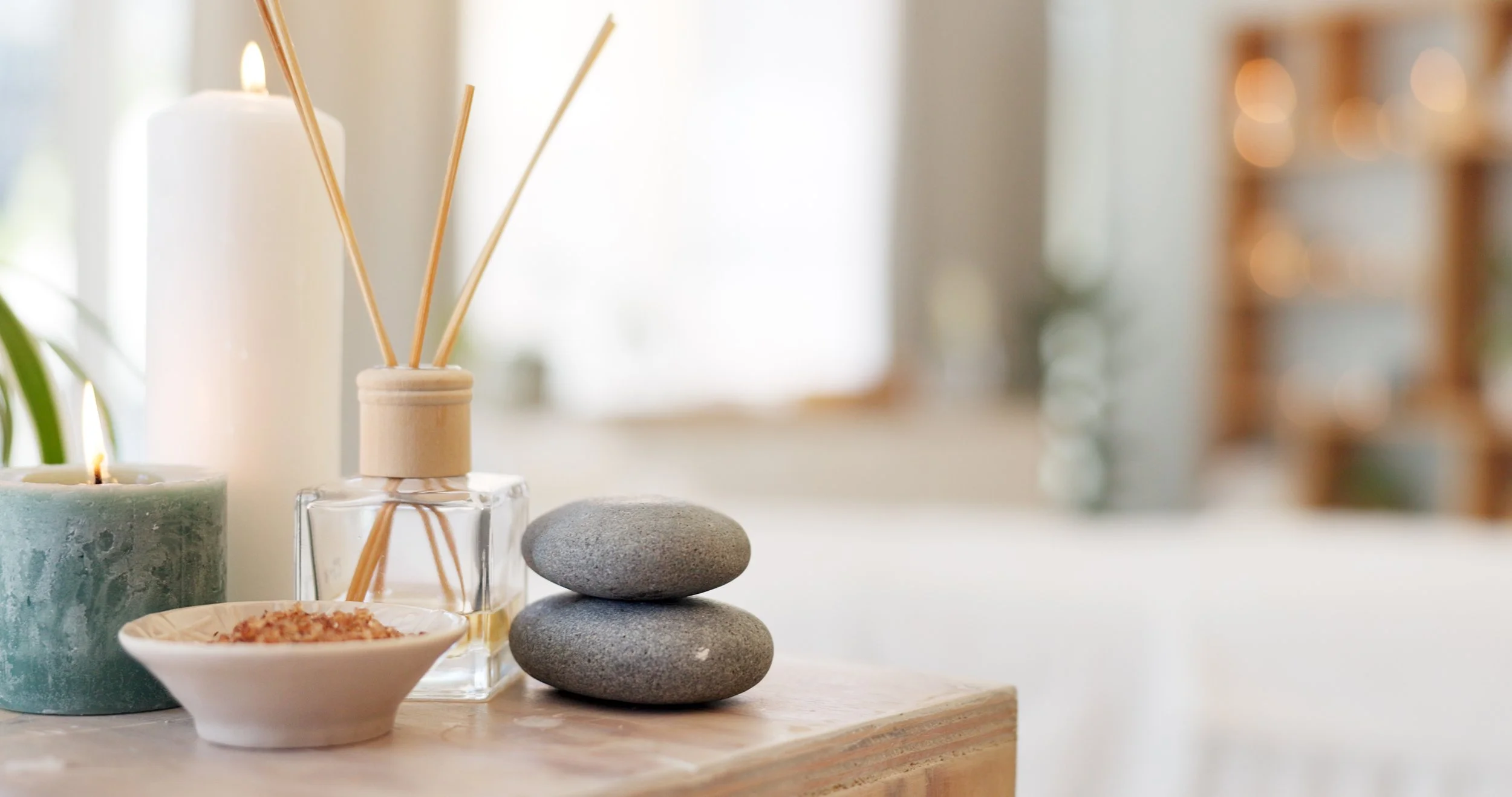 Spa-like setting with candles, incense diffuser, and smooth stones on a wooden surface.