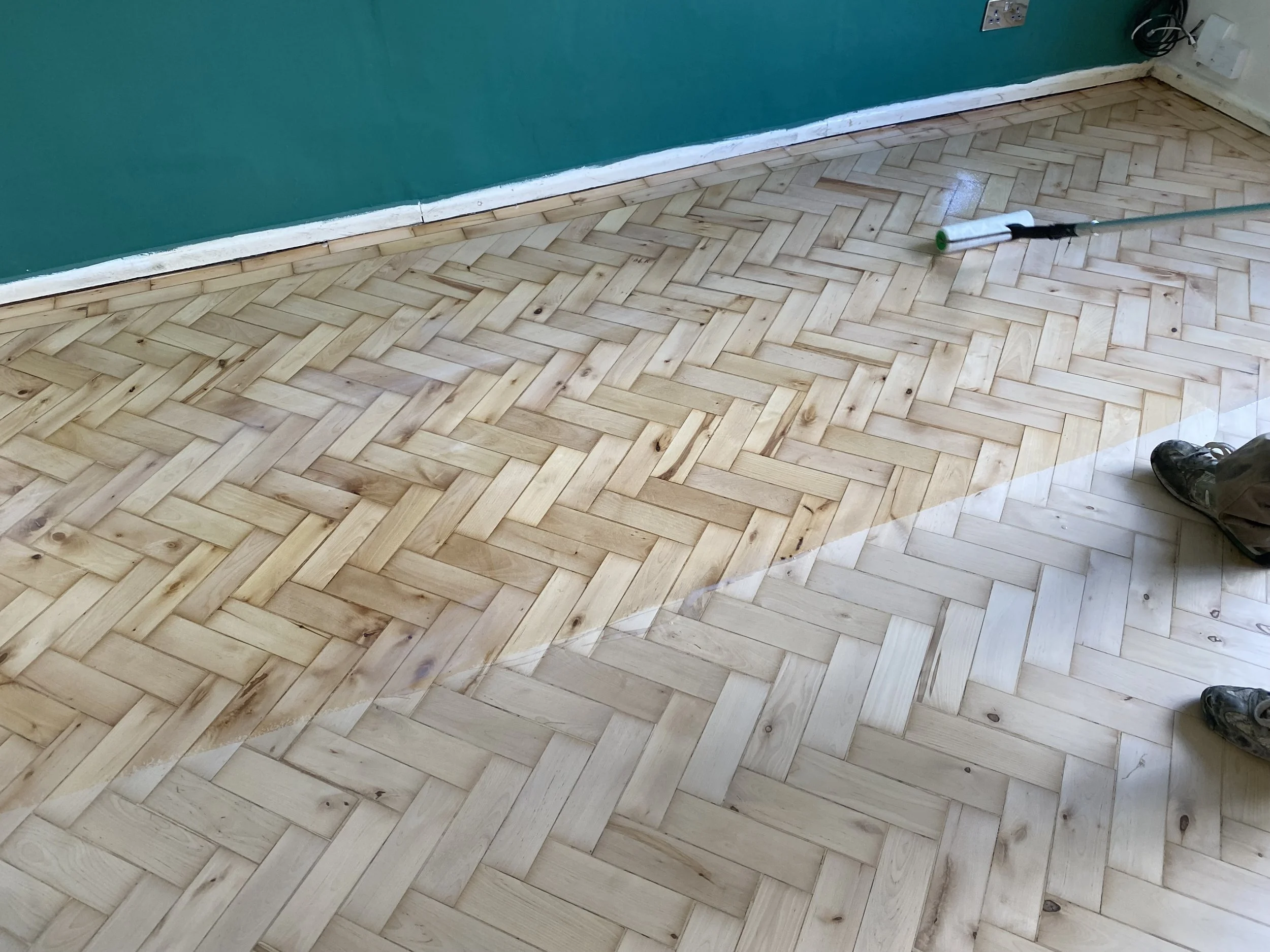 Pine parquet herringbone floor in Solihull, Birmingham, showing the contrast between raw sanded wood and the applied finish during restoration