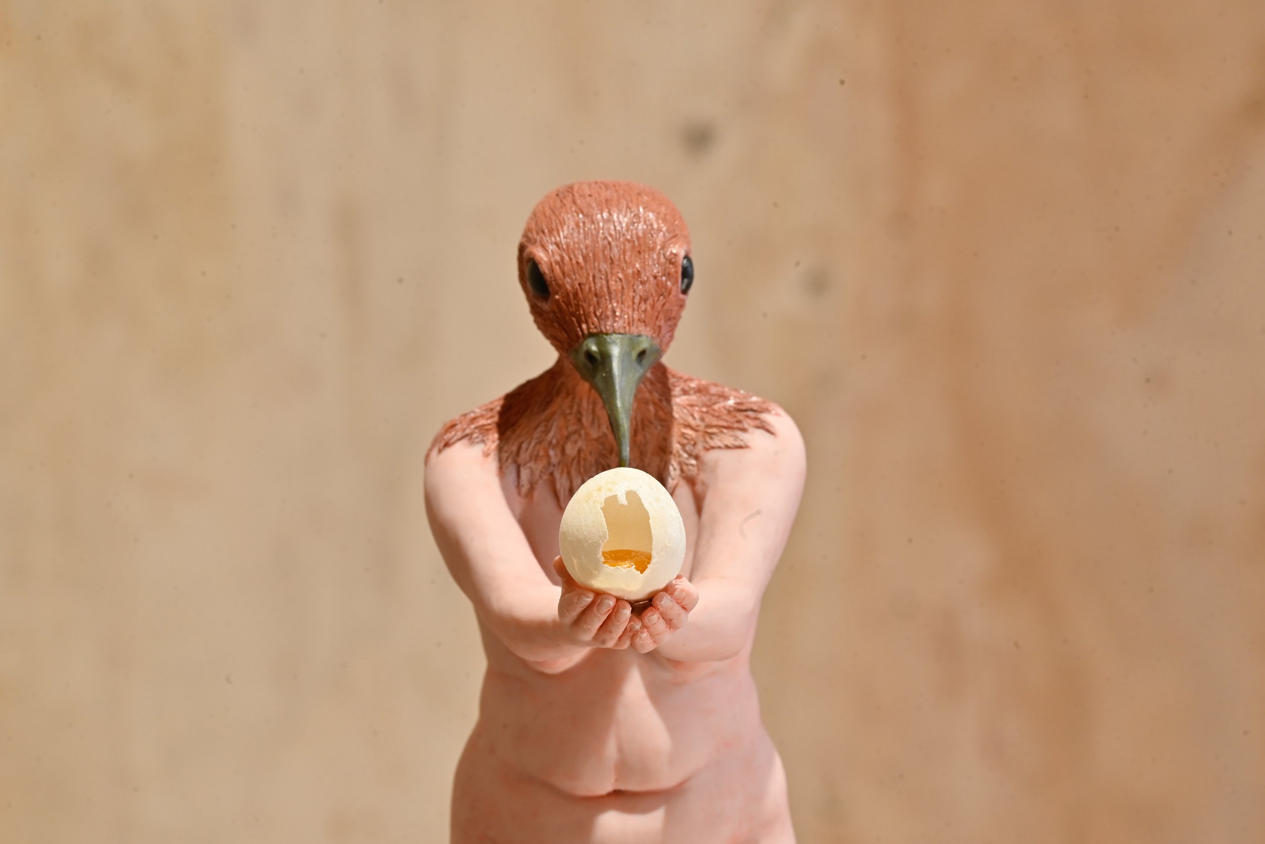 A person with a bird's head holding an eggshell with a bite taken out of it.