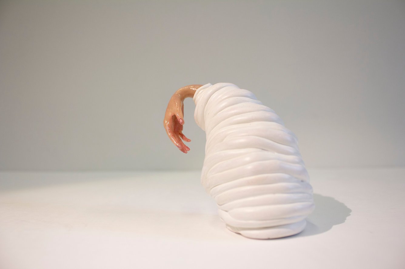 An art sculpture of a worm with a human hand at the front, wrapped in a spiral white shell shape.