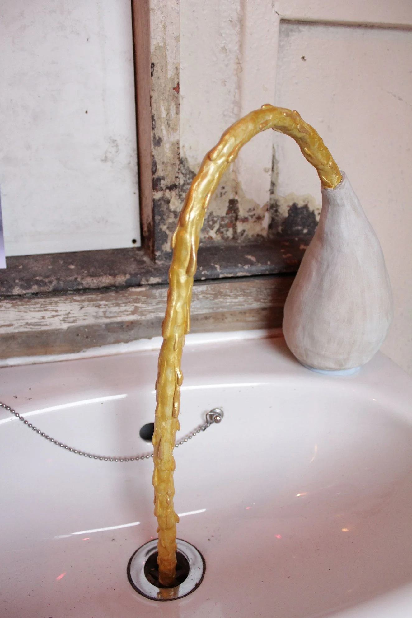 white ceramic vase with yellowish water flowing,  positioned over a sink