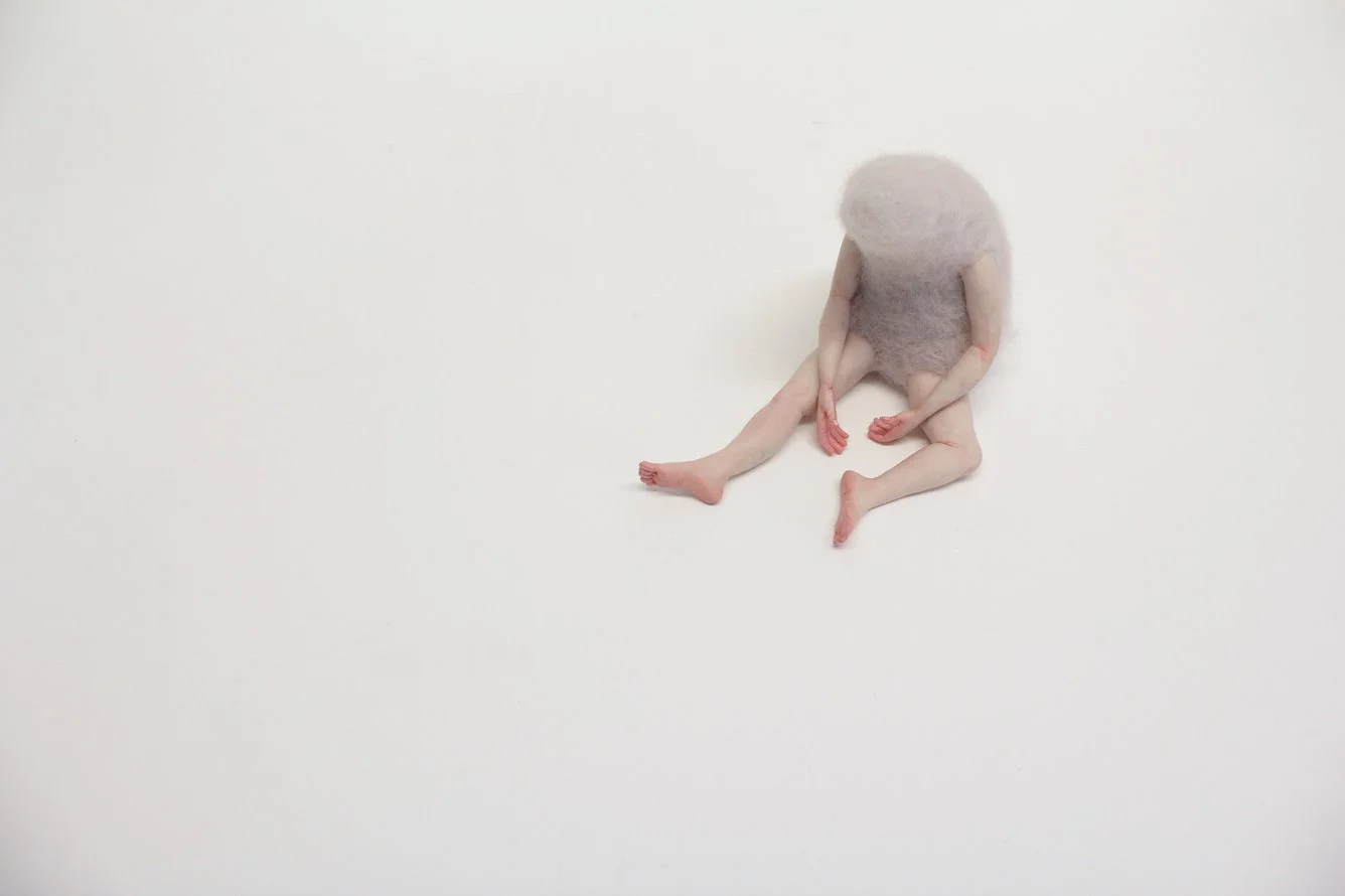 An abstract creature with the body of a human baby and a fuzzy animal head sitting against a plain white background.