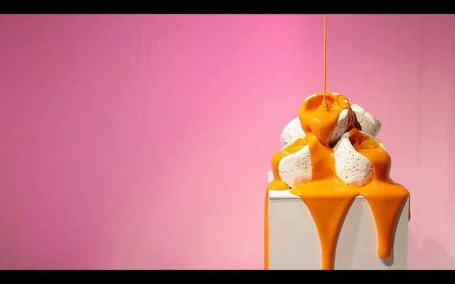 A white pedestal displays a pink and white ceramic vase with pink paint dripping down the side.