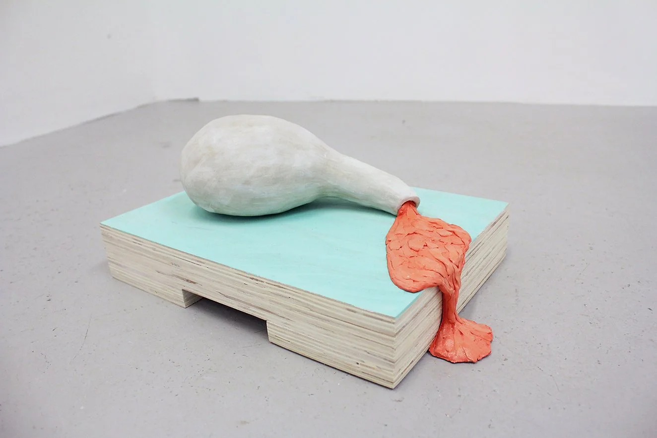 A sculpture of a white and gray ceramic sculpture with a dripping substance, placed on a light blue rectangular base, on a gray surface against a white wall.