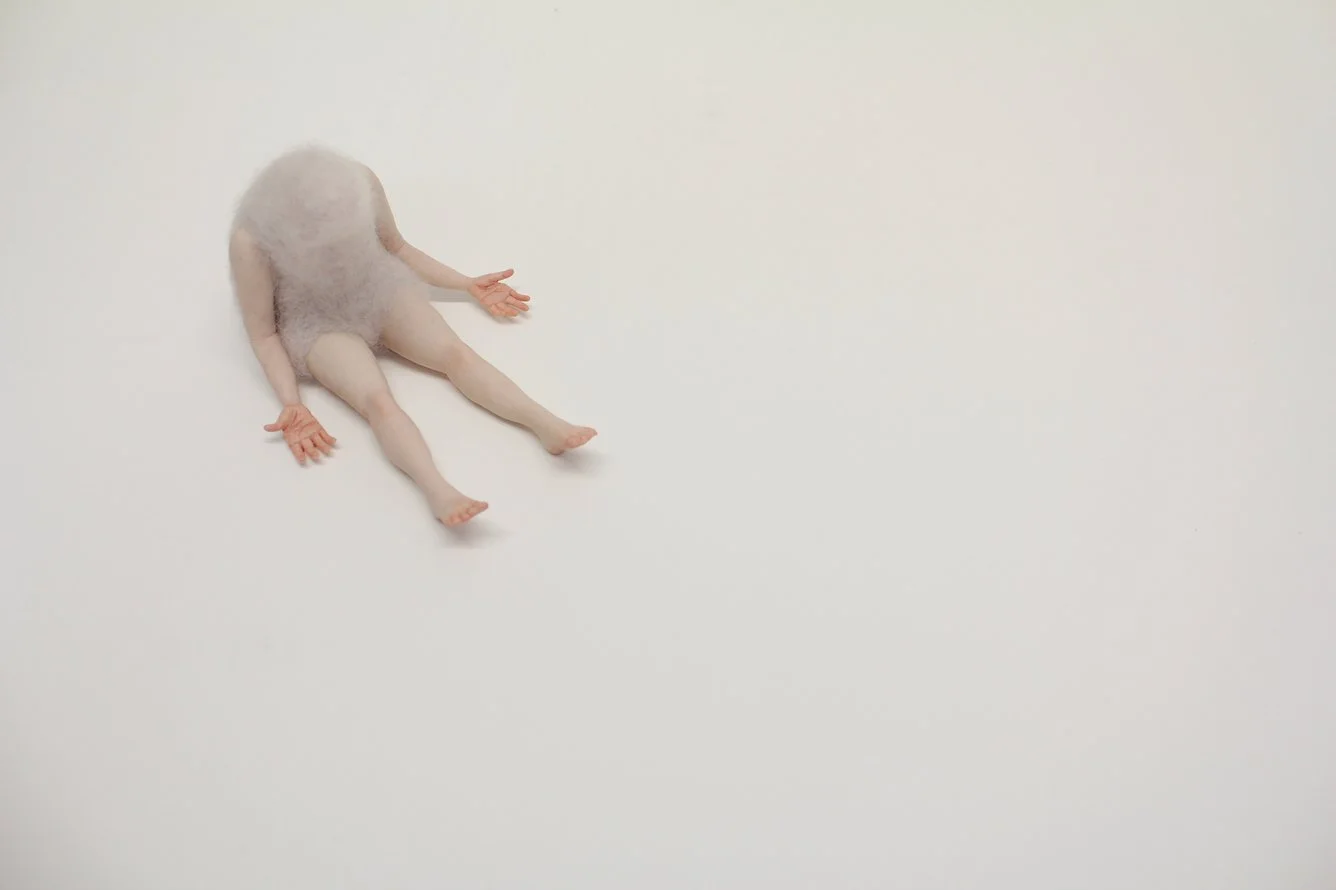 A handmade felted figuring sitting on the a while surface with left slightly parted and has splayed out.