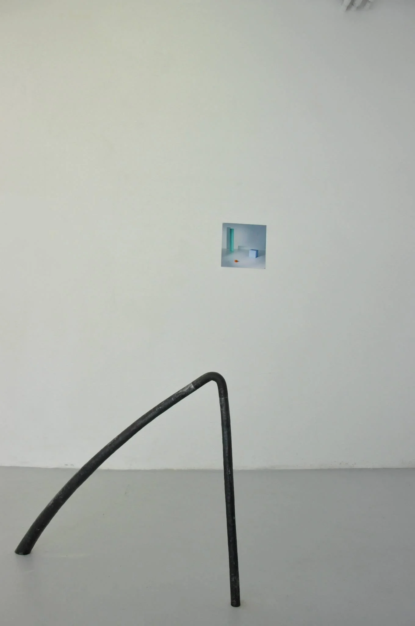 A minimalist art installation with a bent metal rod on a gray floor, a small square opening in a plain white wall showing a colorful abstract scene.