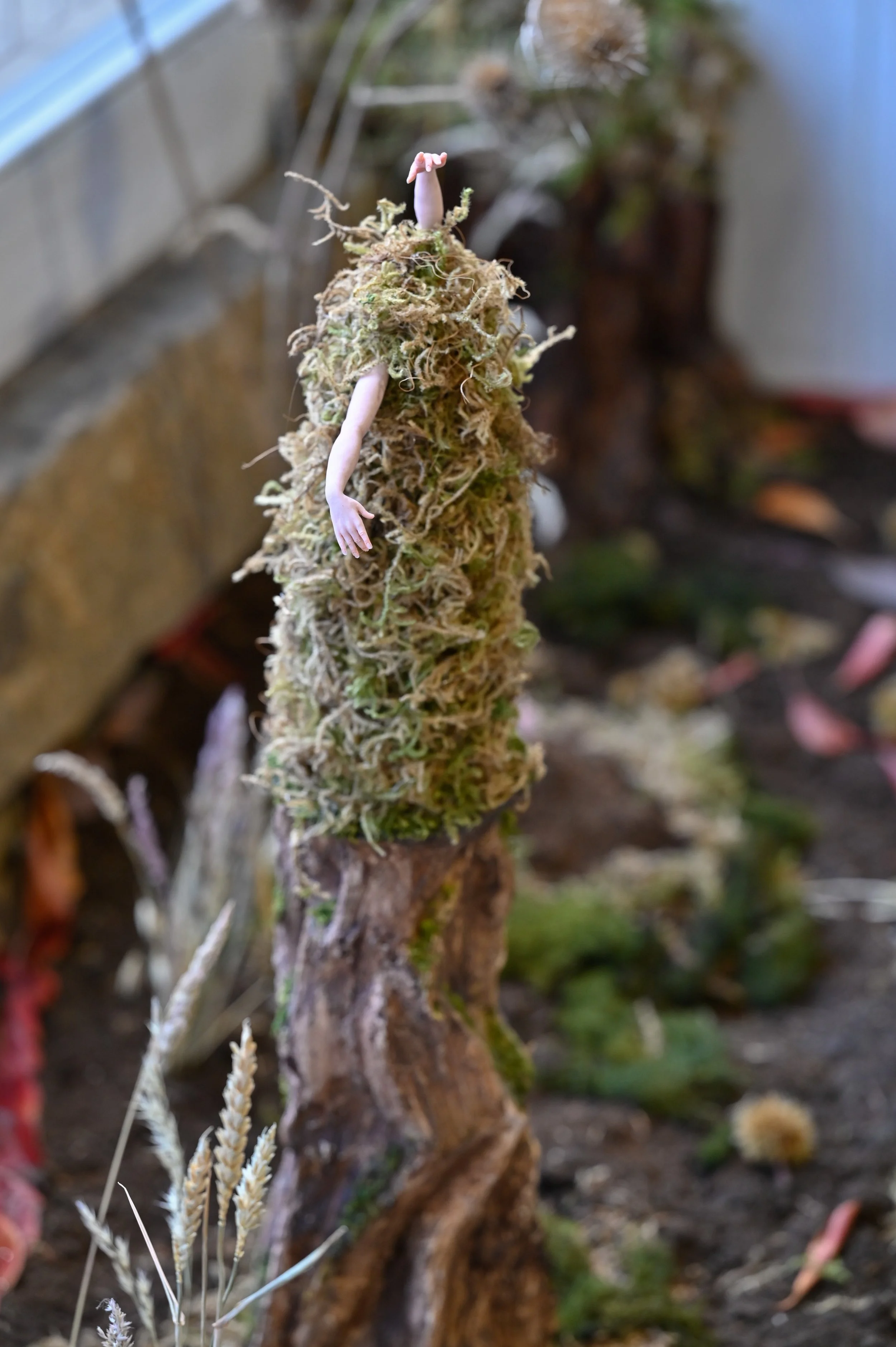 A moss mound with a small, disembodied human arm and hand extending from the side and reaching out.
