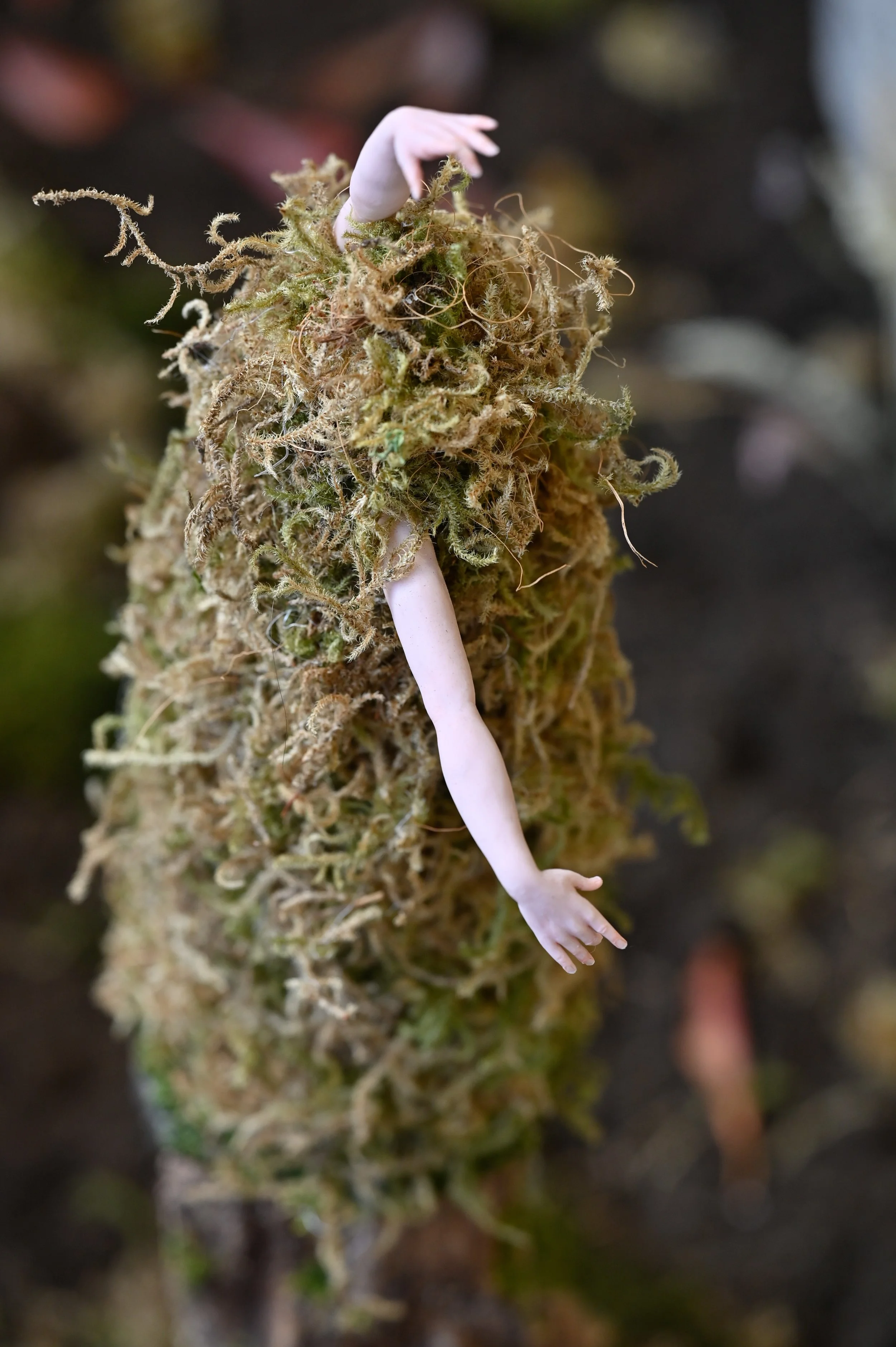 A moss mound with a tiny, realistic-looking sculpted polymer clay arm and hand attached to it.