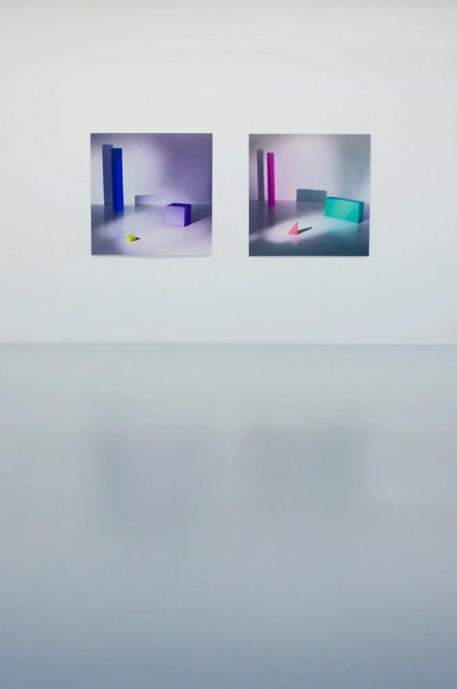 Two abstract art pieces with geometric shapes and colorful blocks on a white gallery wall.