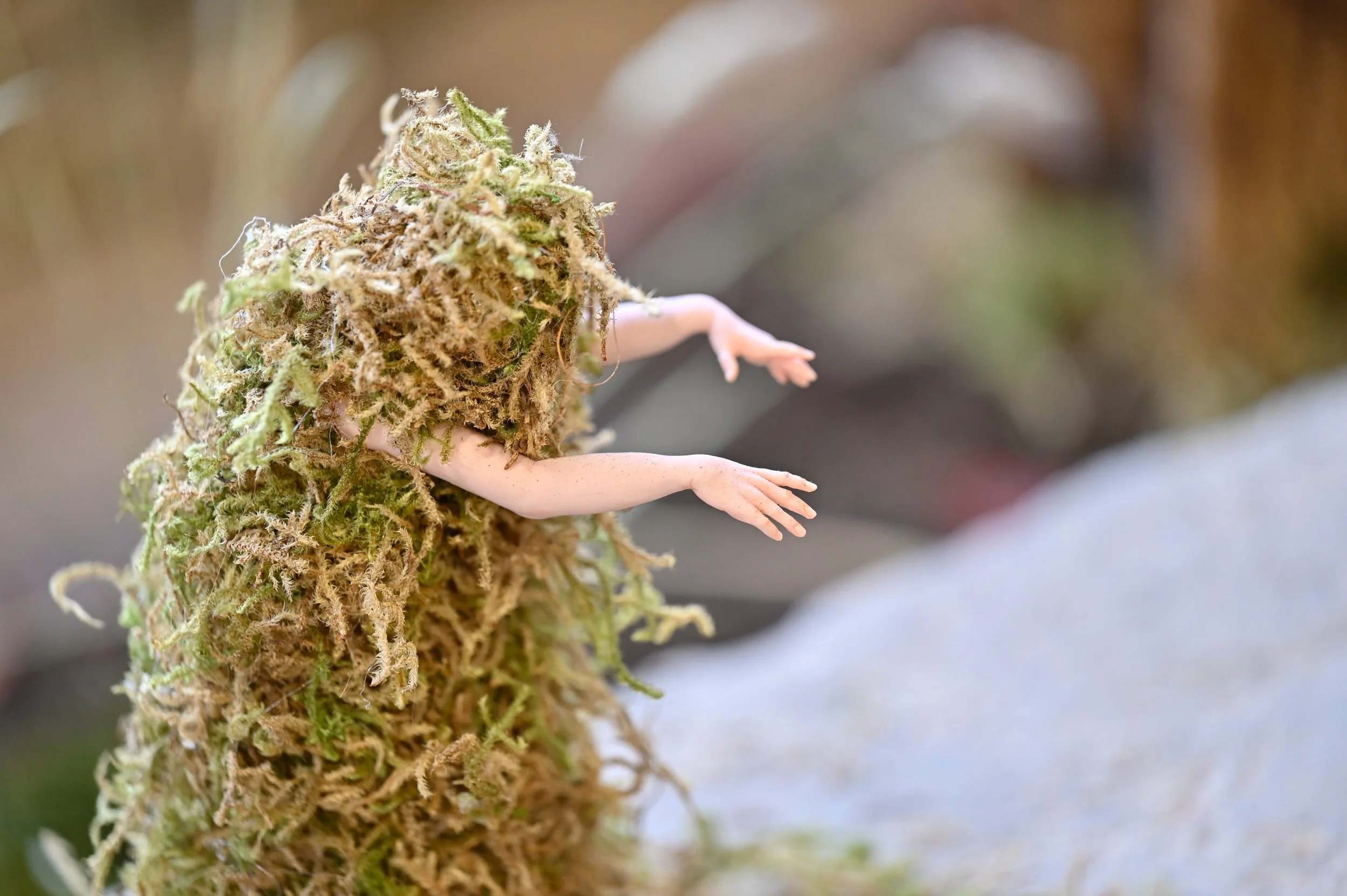 Close-up of  a tiny human figurine covered in moss, giving the illusion of a miniature person climbing or hanging from the plant.