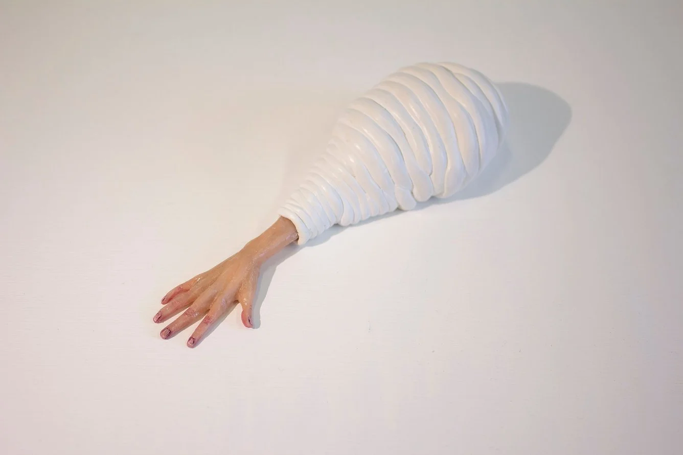 Unusual sculpture resembling a arm with five fingers, wrapped in white material, placed on a plain white surface.