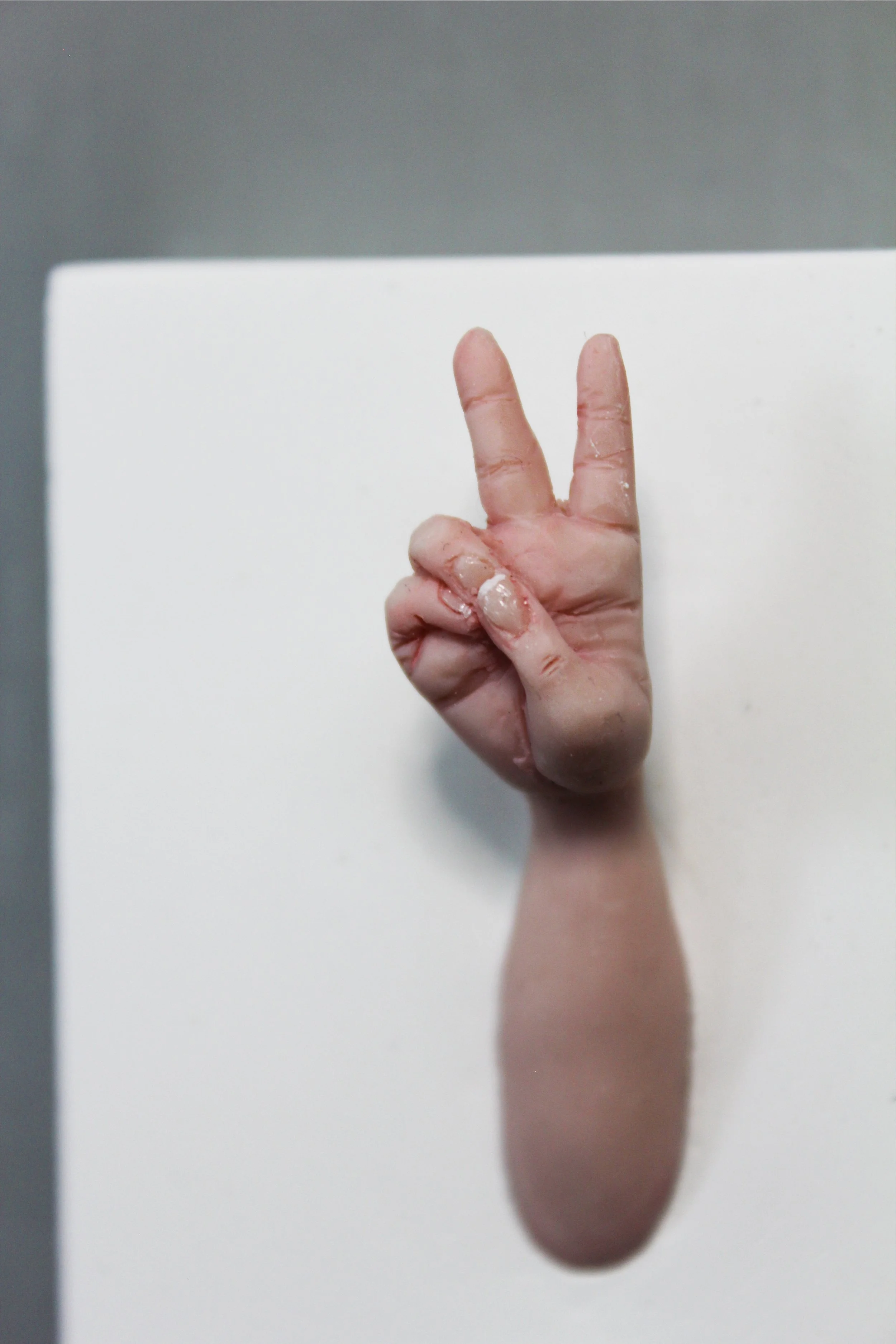 A hand making the peace sign with two fingers, emerging from a flat surface, creating a shadow resembling an elongated oval.