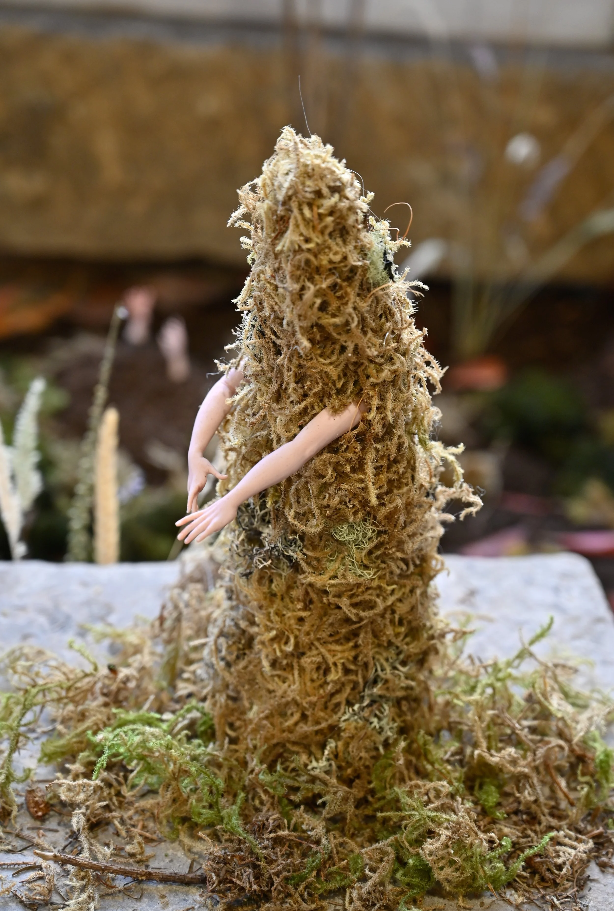 A close-up of a moss humanoid with sculpted polymer clay arms attached to it.