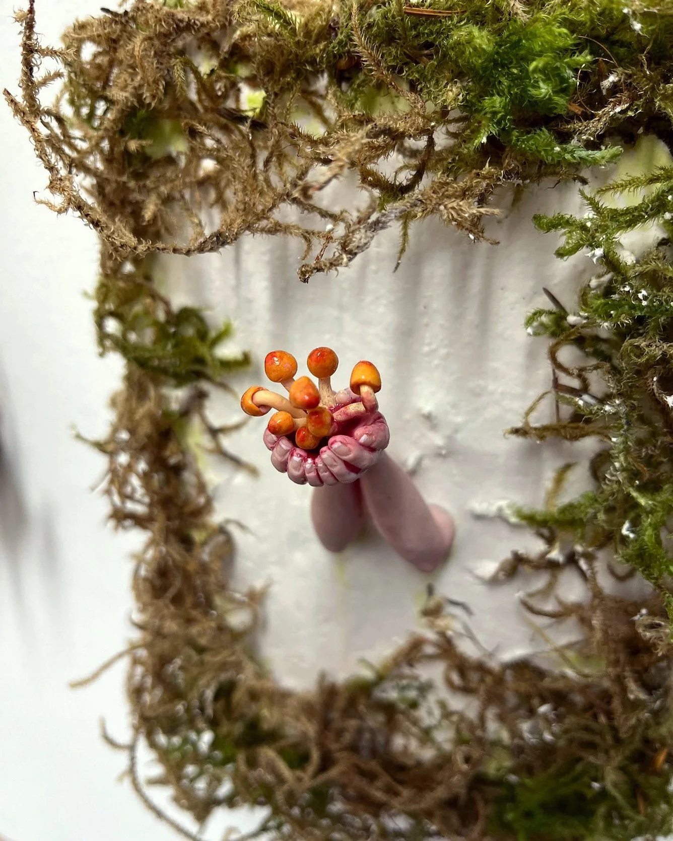 An arts installation with hands holding tiny mushrooms, enclosed by a circle of moss and plant material.