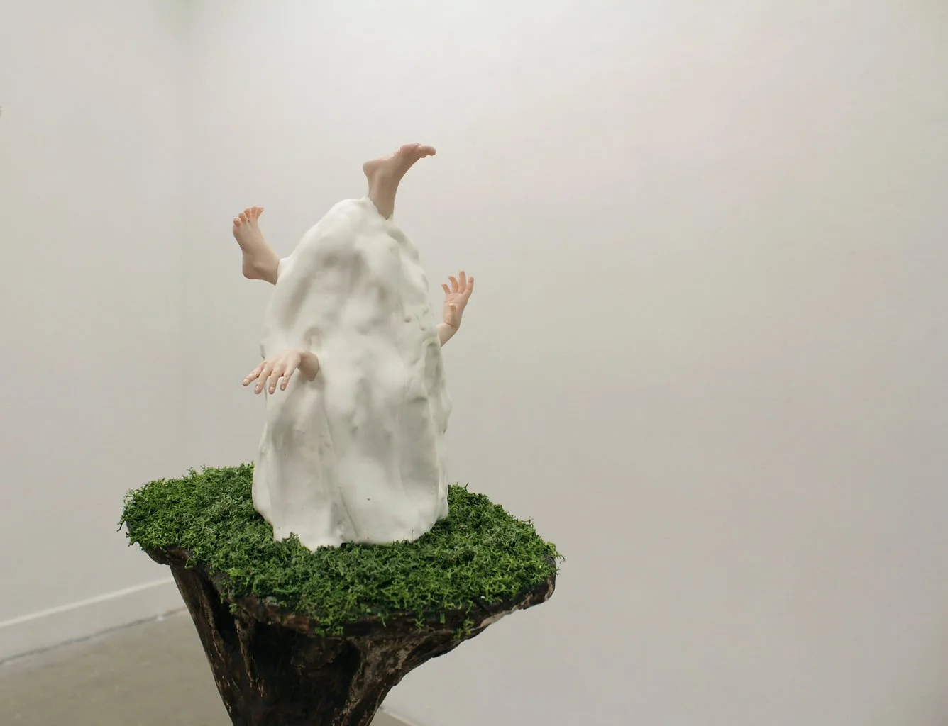 Sculpture of a humanoid robot emerging from a white cloud-like form, with multiple human hands reaching out, placed on a moss-covered wooden base.