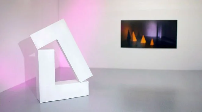 An art gallery with a white abstract sculpture on the left and a digital display of orange geometric shapes on the wall in the background.