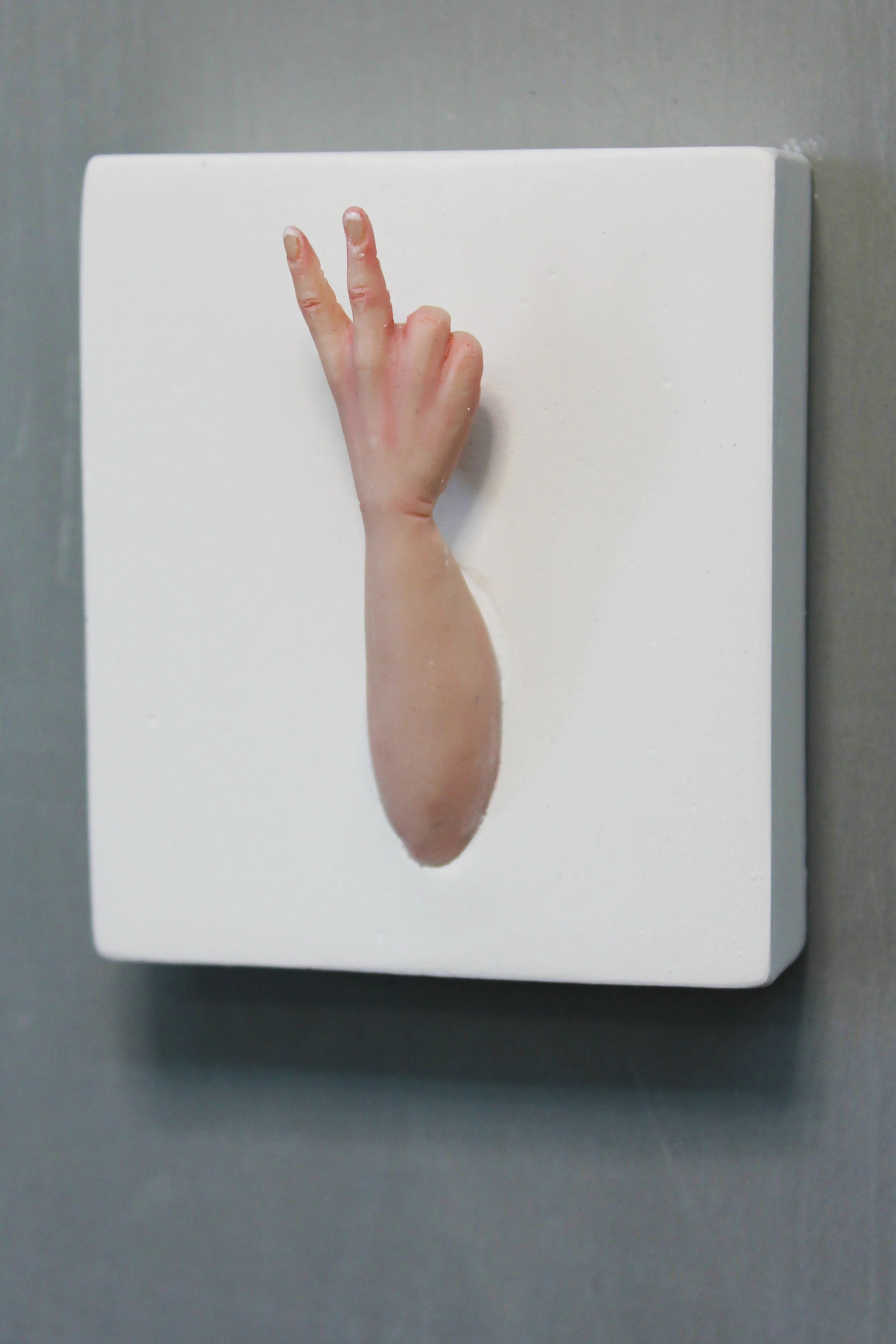 An artwork on a gray wall depicts a human hand and arm reaching out from a hole, with the hand making a peace sign.