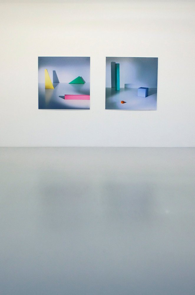 Two abstract art prints featuring colorful geometric shapes hung on a white gallery wall.