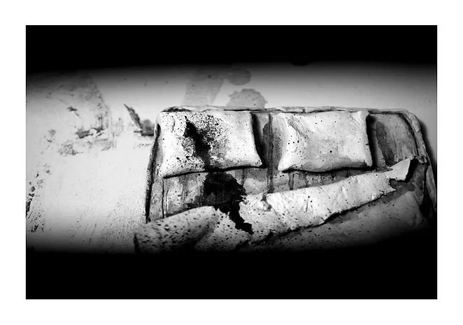 A broken mattress and pillows with stains and damage, set against a wall with peeling paint.