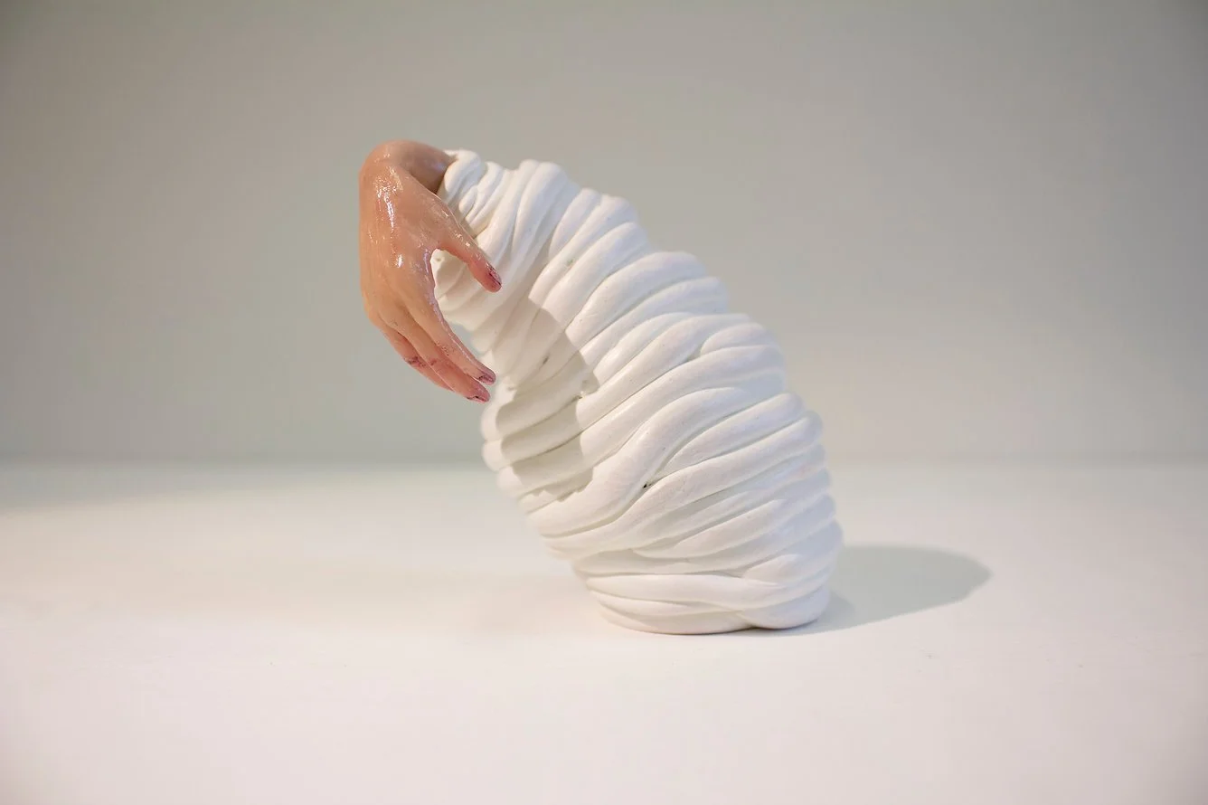 A sculpture resembling a seashell with a human hand emerging from its opening, painted in flesh tones.