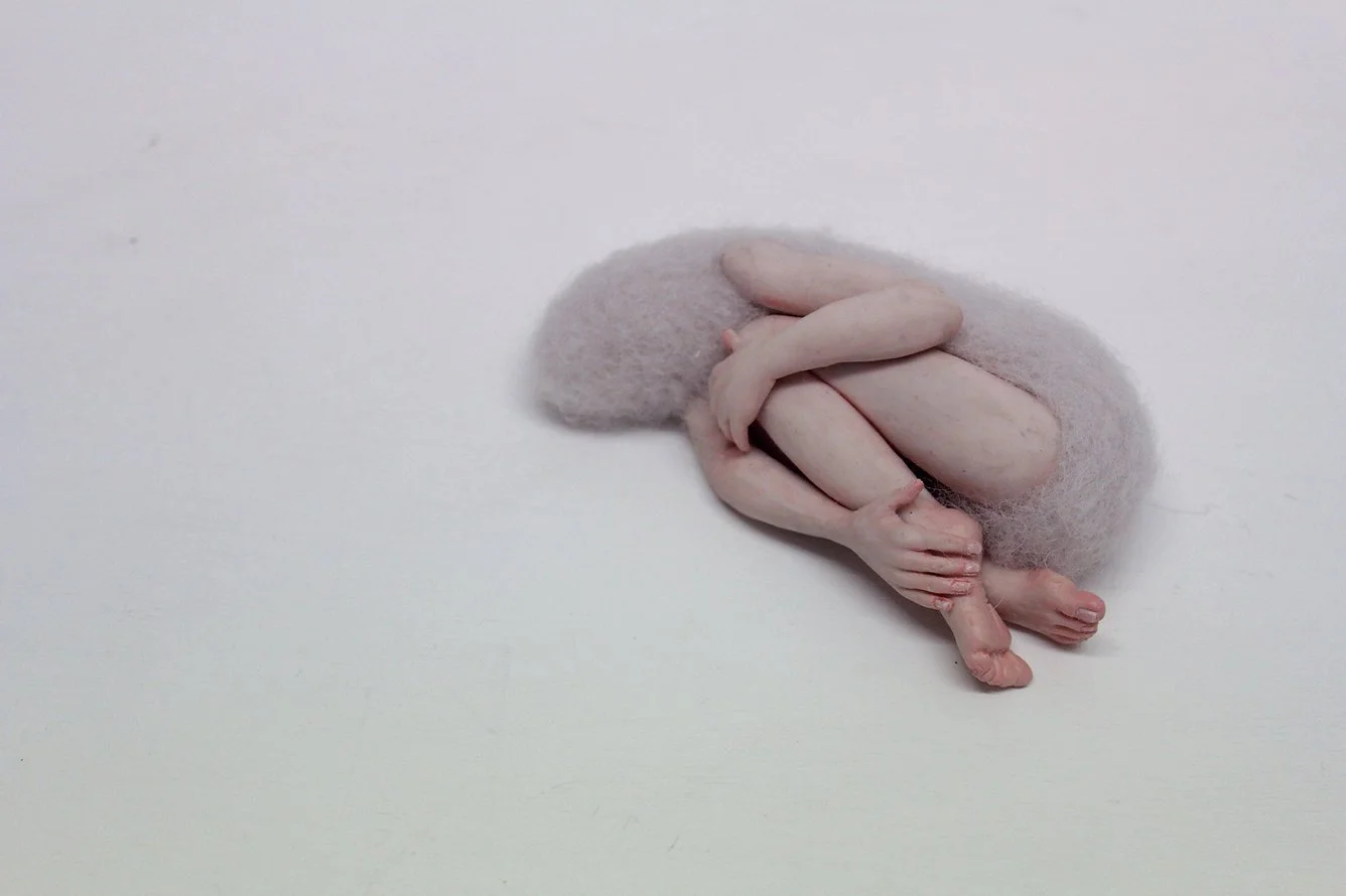 A tiny, hairless, white rodent curled up on a white surface, with a fuzzy tail and small limbs tucked close to its body.