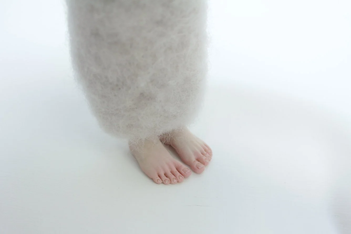 Close-up of a person's feet with toes, partially covered by a soft, fuzzy, light-colored garment or blanket.