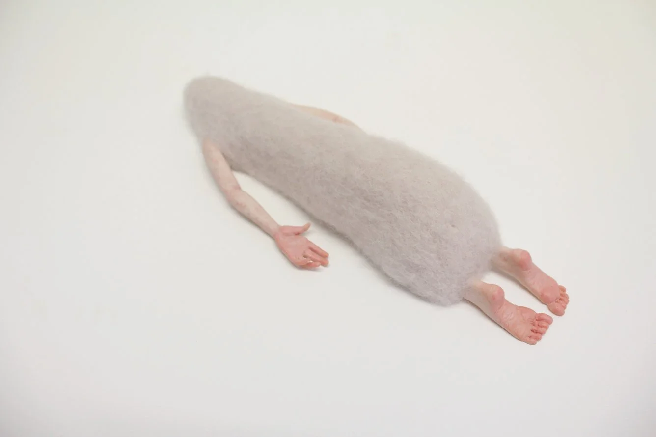 A felted figurine a white body and pink limbs on a white background.